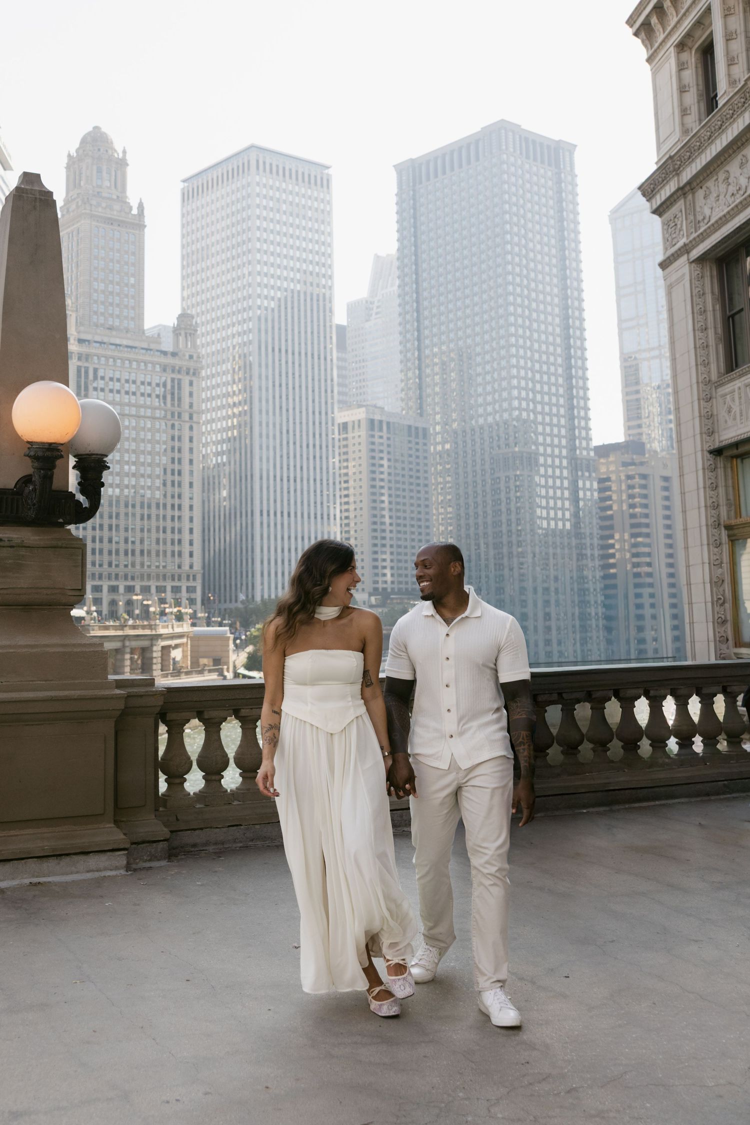 A couple strolls along a city balcony with Chicago's magnificent skyline rising in the background.