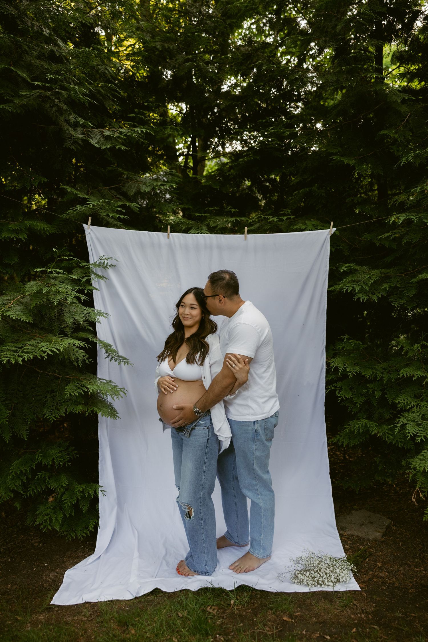 A sweet maternity photography session with a couple barefoot against a white backdrop outdoors.