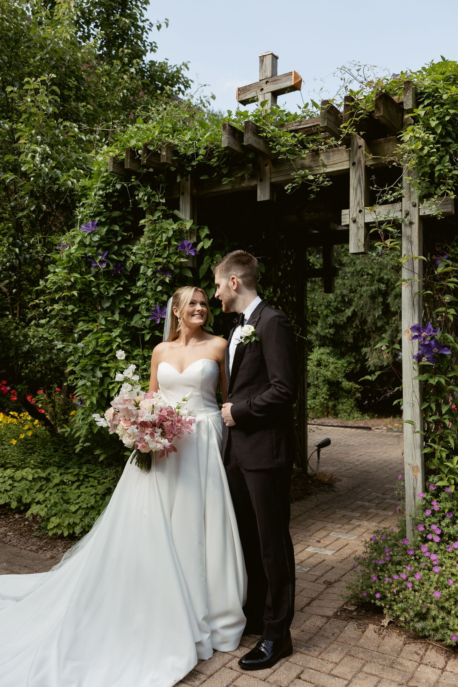 Newlyweds pose for romantic portraits in a beautiful garden setting with blooming flowers.