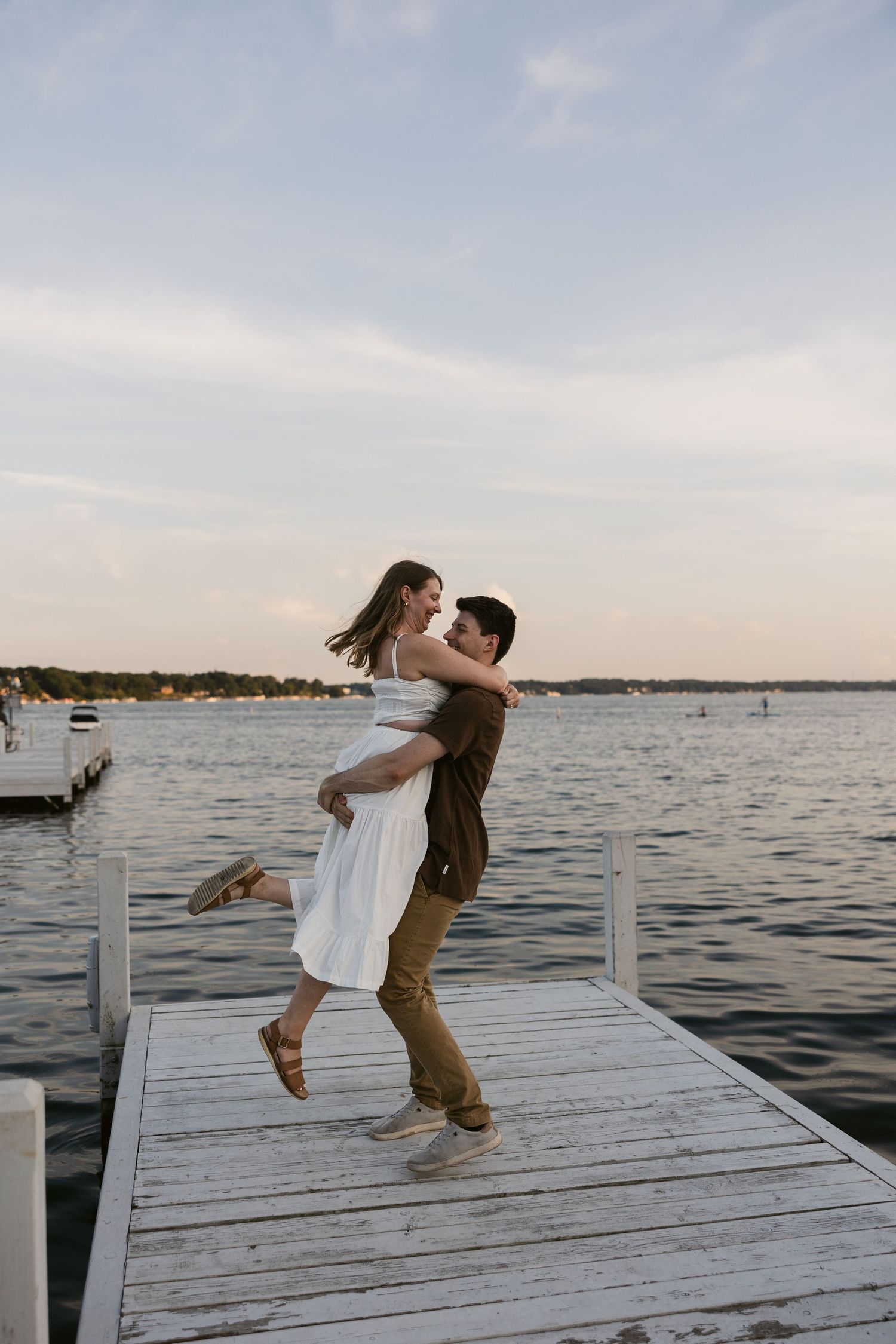 Playful moment captured on a lakeside dock as couple dances together.