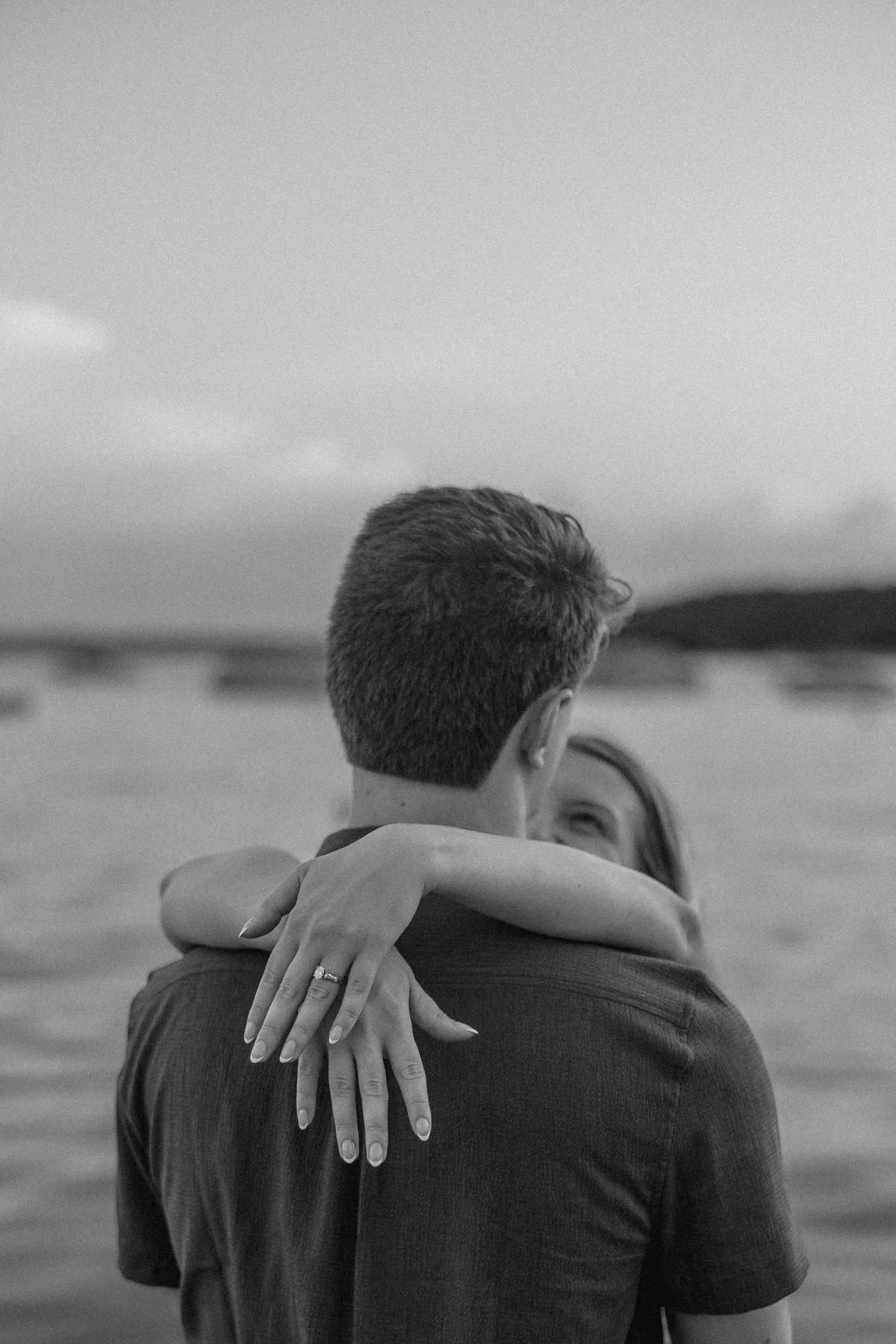 A black and white intimate portrait of a couple embracing by the ocean.