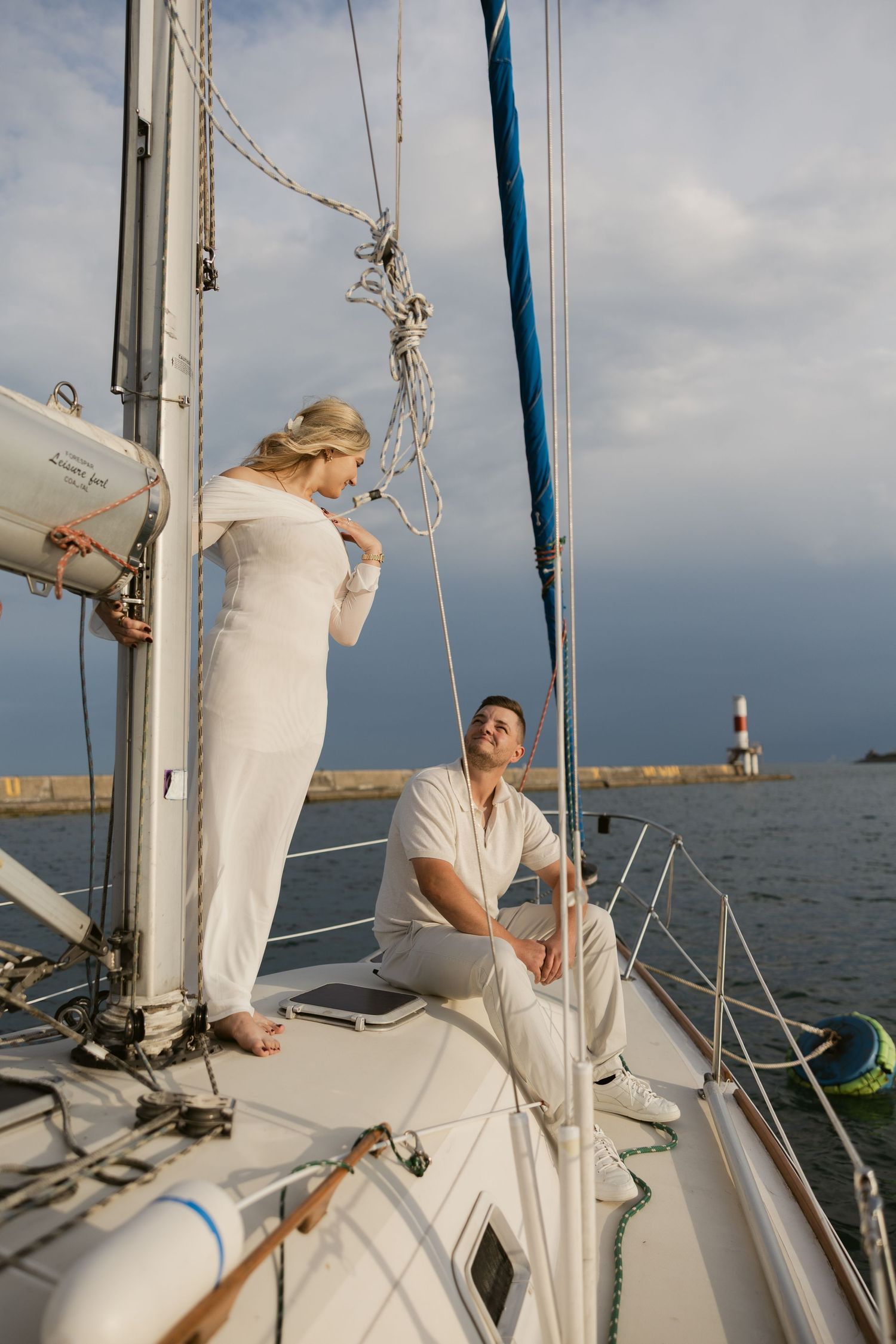 A couple enjoying a peaceful moment aboard a sailboat with a lighthouse visible in the distance.