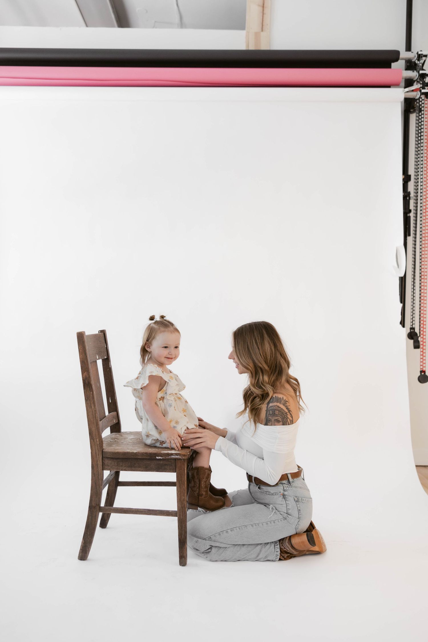 Studio photoshoot showing a tender moment between two people with a wooden chair on white backdrop.
