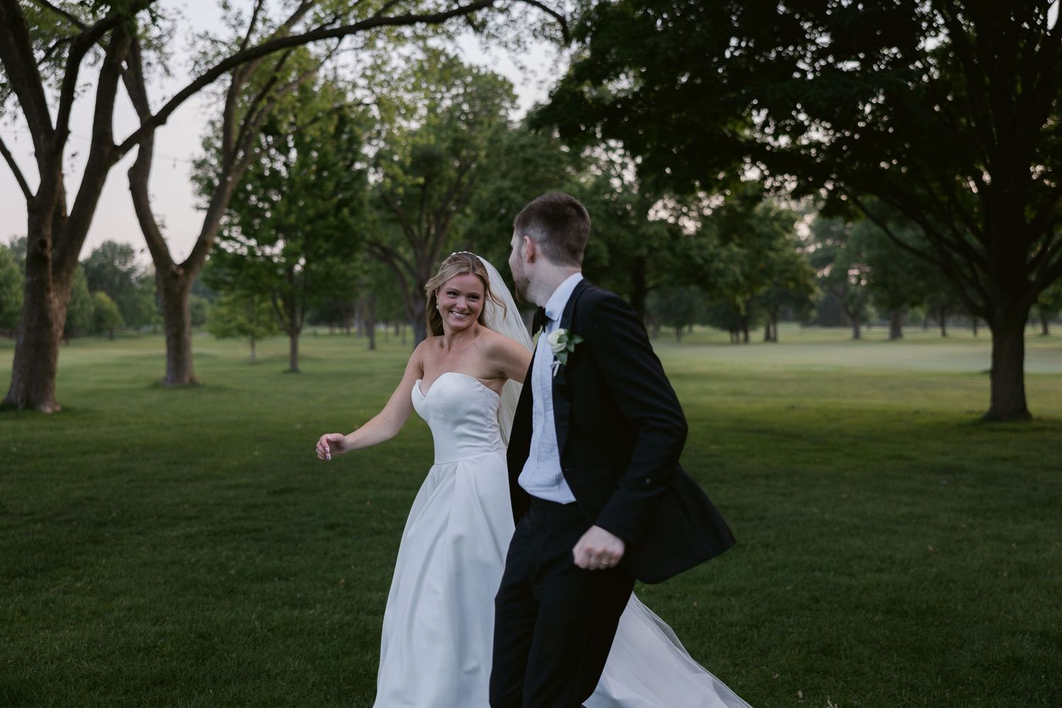 Wedding couple shares joyful moments on lush green grounds at sunset.