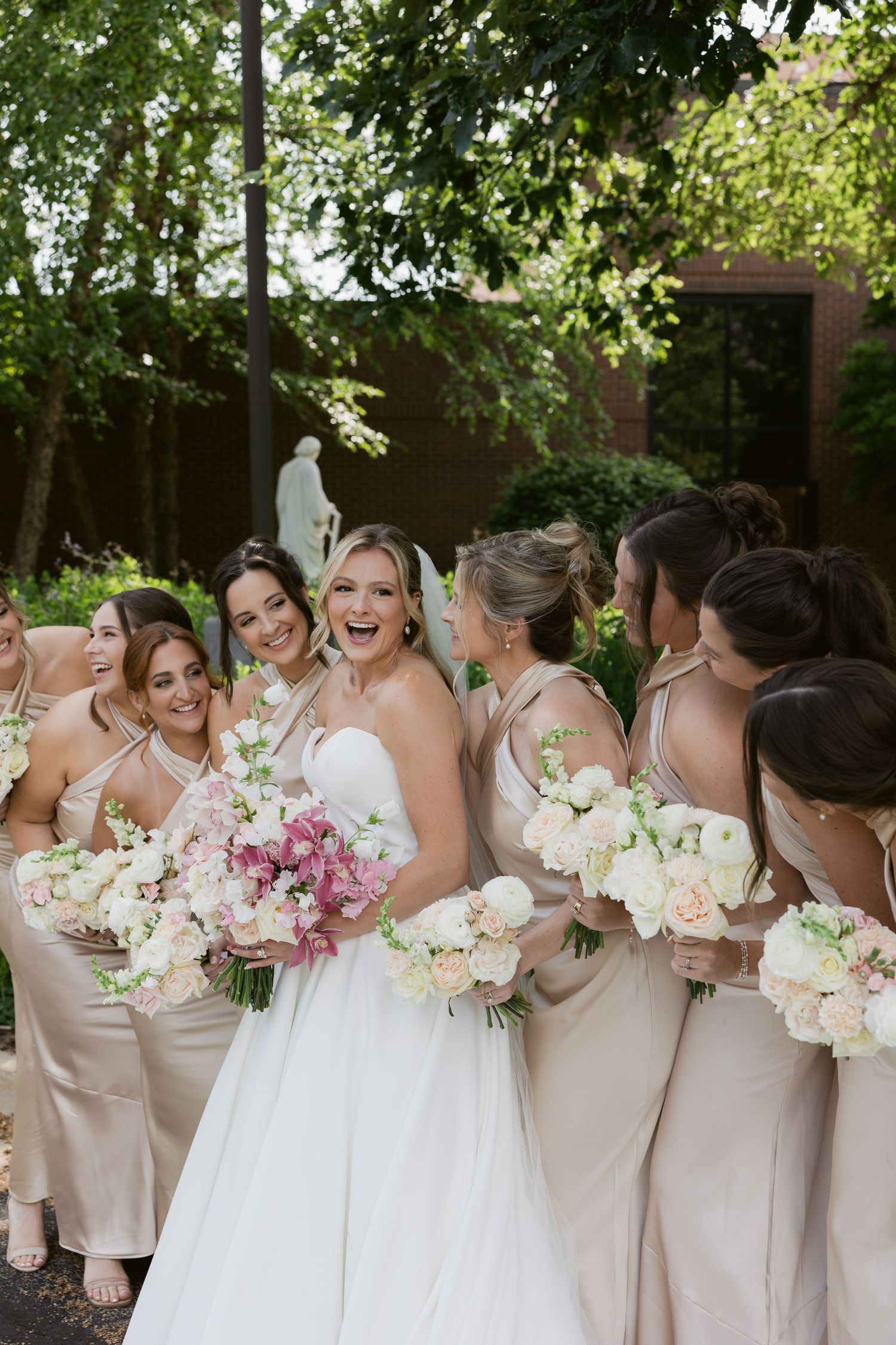 Bridesmaids in champagne dresses celebrating with the bride holding pink and white bouquets.