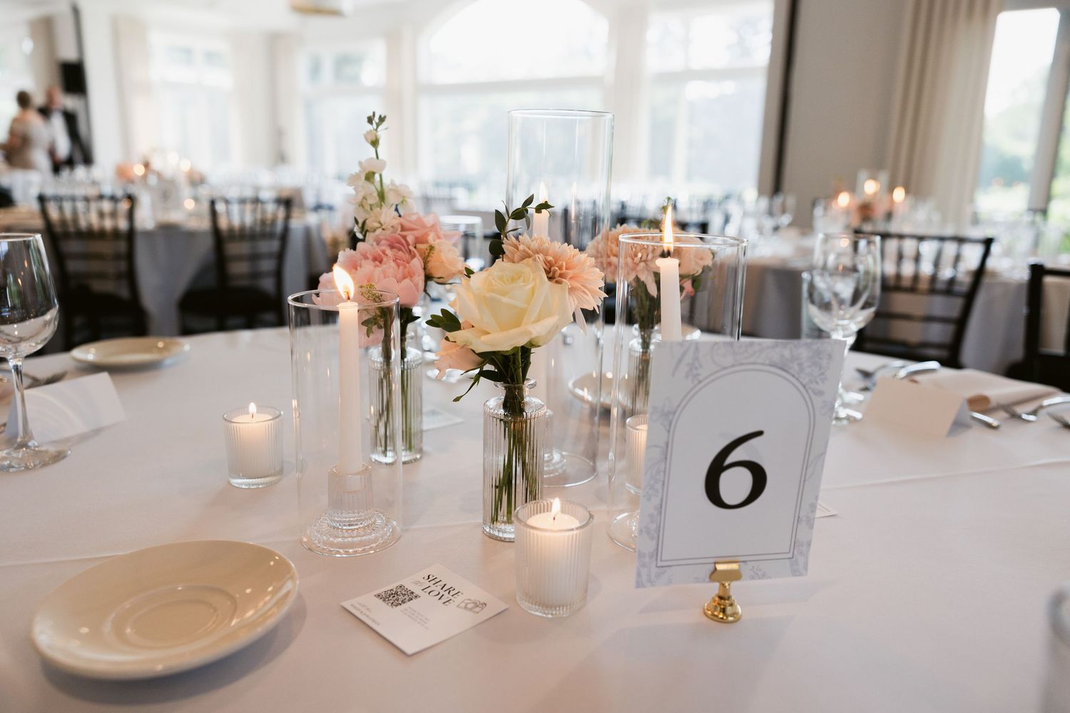 An elegant wedding reception setup with white table settings, candles and minimalist floral centerpieces.