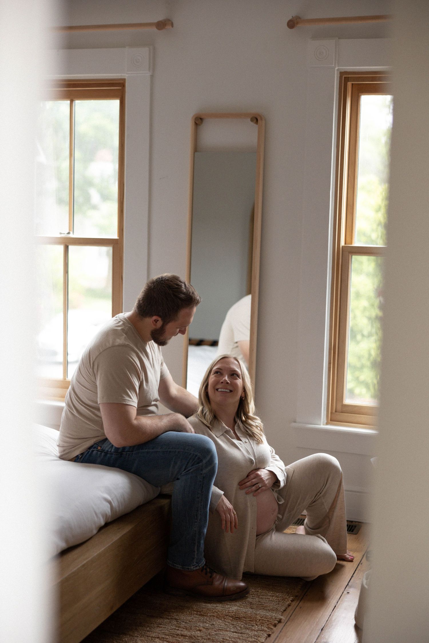 An intimate moment captured in a sunlit bedroom with natural wood accents and white bedding.