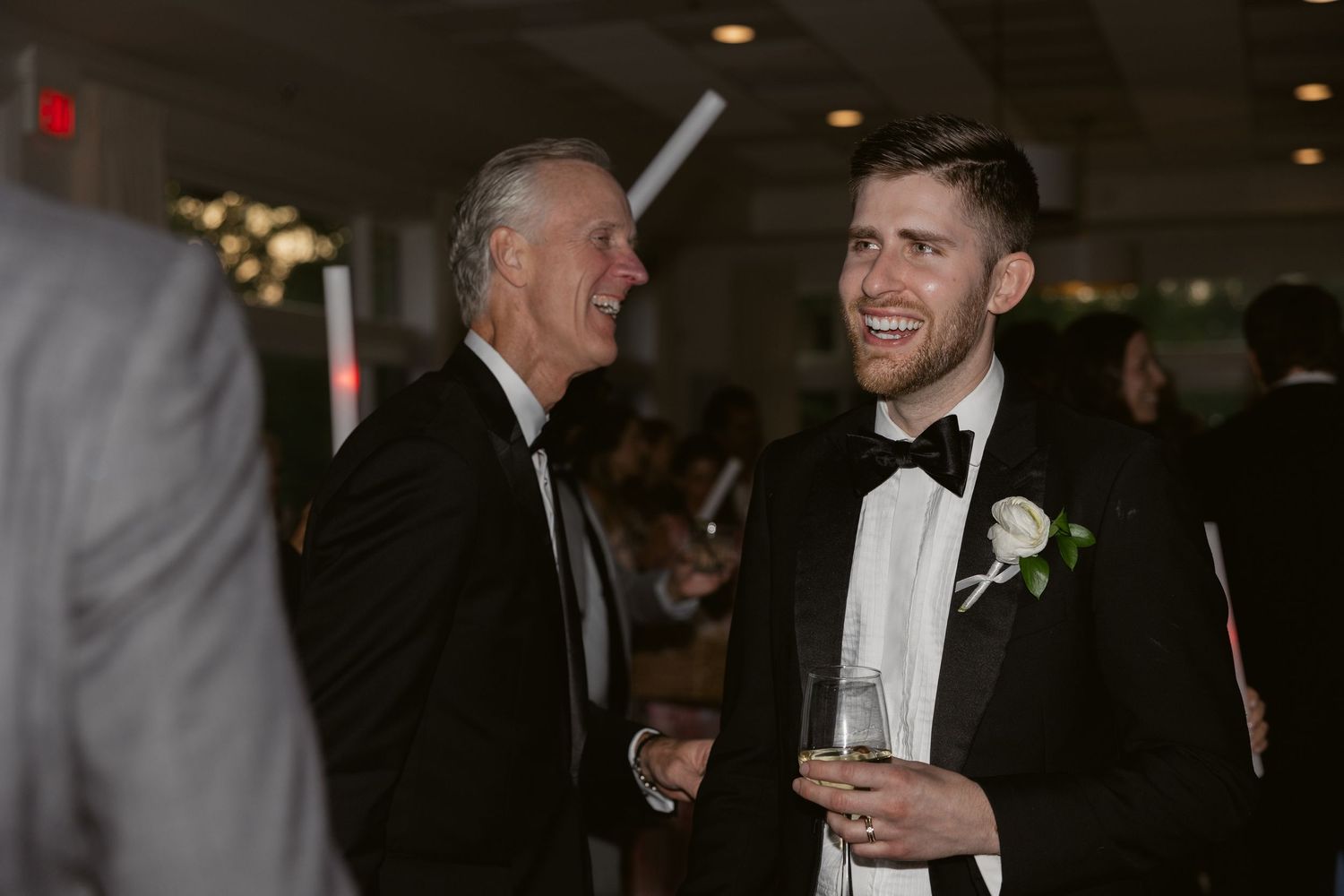 Father and son share a laugh during a formal evening reception at a suit-and-tie event.