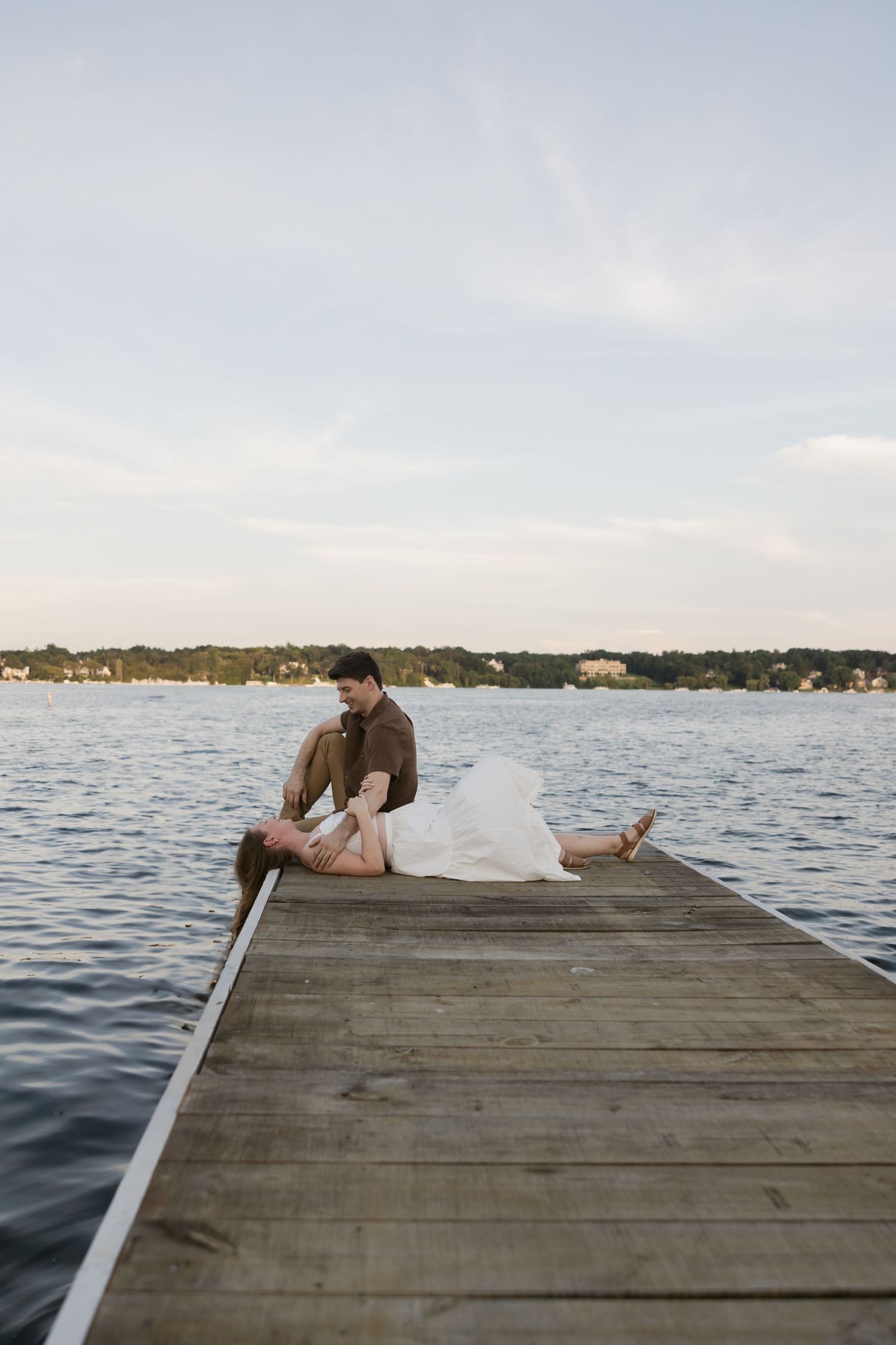 A couple relaxing together on a wooden dock overlooking a serene lake at sunset.