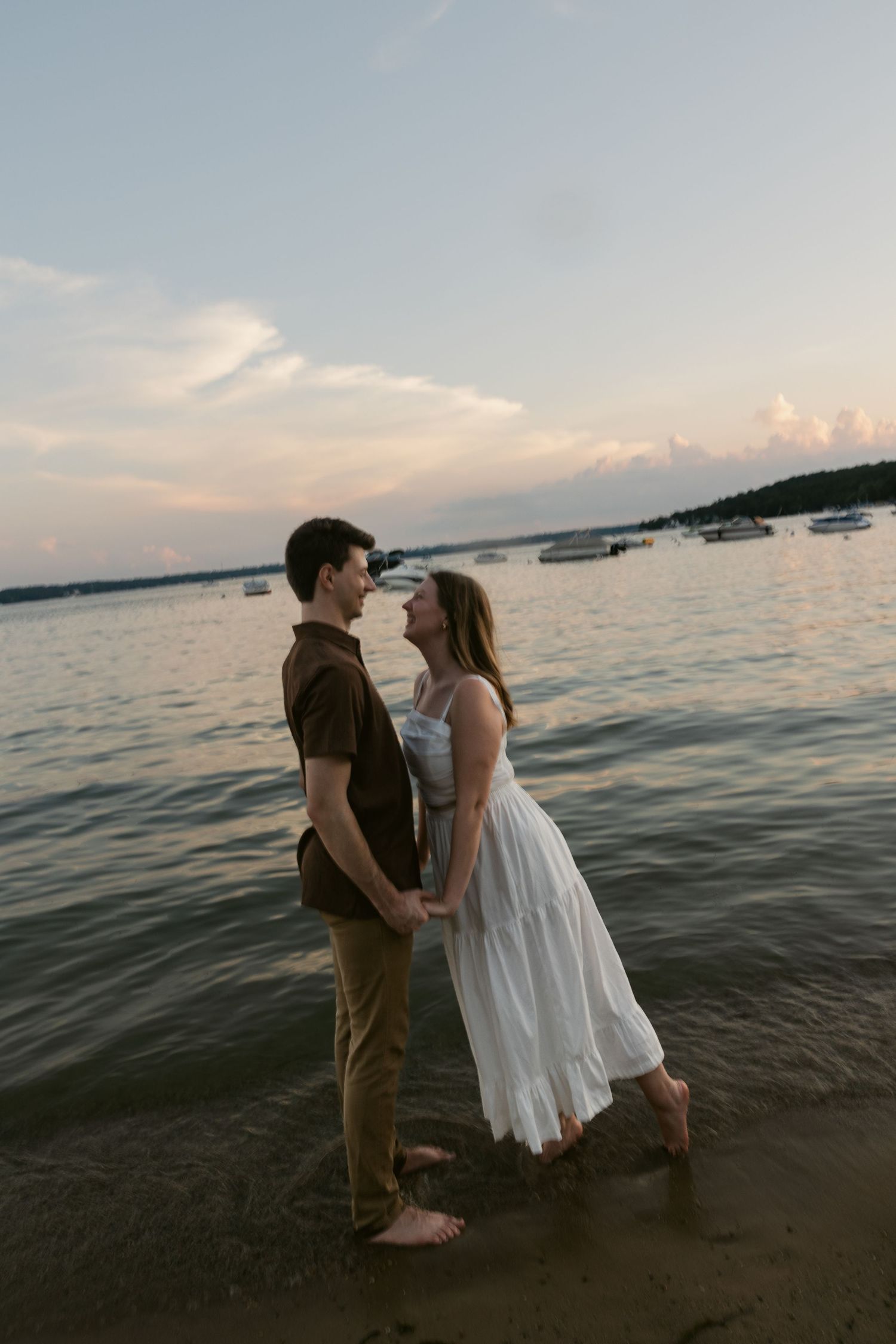Two figures sharing a romantic moment along the beach at sunset with boats visible in the distance.