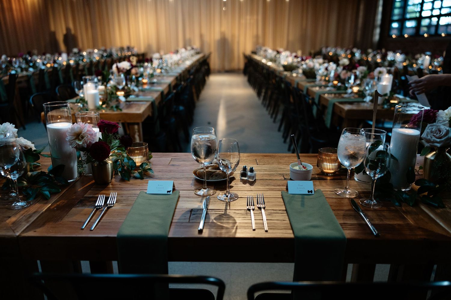 Elegant wedding reception table setup with modern place settings and moody lighting in wood-paneled room.