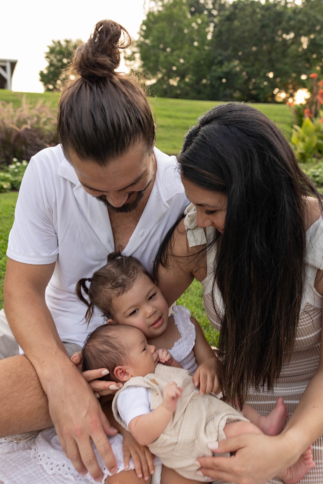 An intimate family moment captured as parents cuddle with their young children on a summer day.