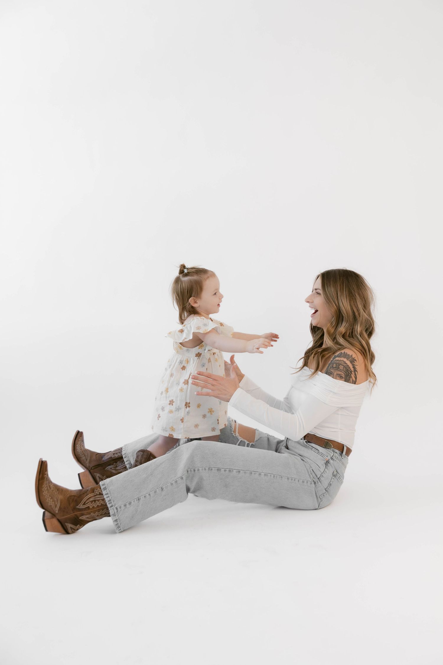 Two people play and interact while sitting on floor during a minimalist studio photoshoot.