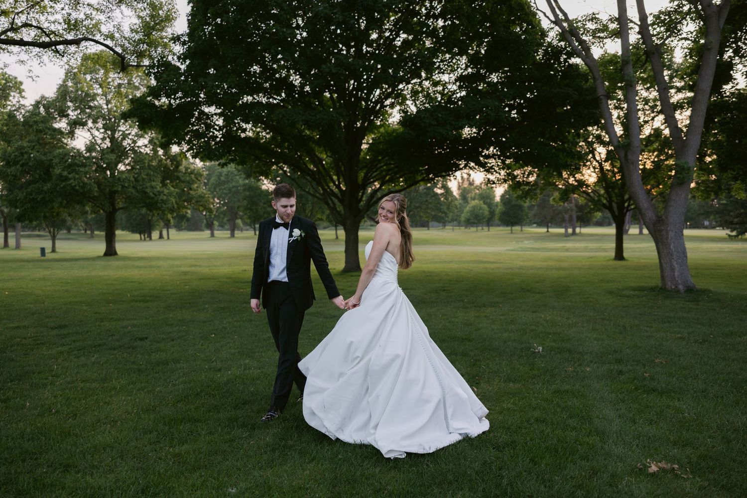 Sunset wedding portraits taken on a sprawling green lawn with trees in background.