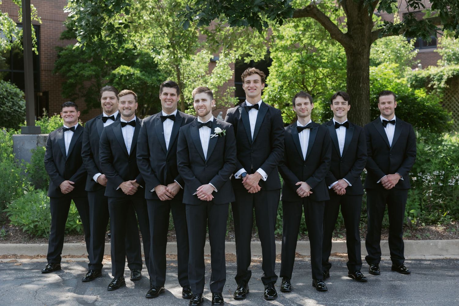 Wedding party groomsmen lined up outdoors wearing classic black tuxedos.