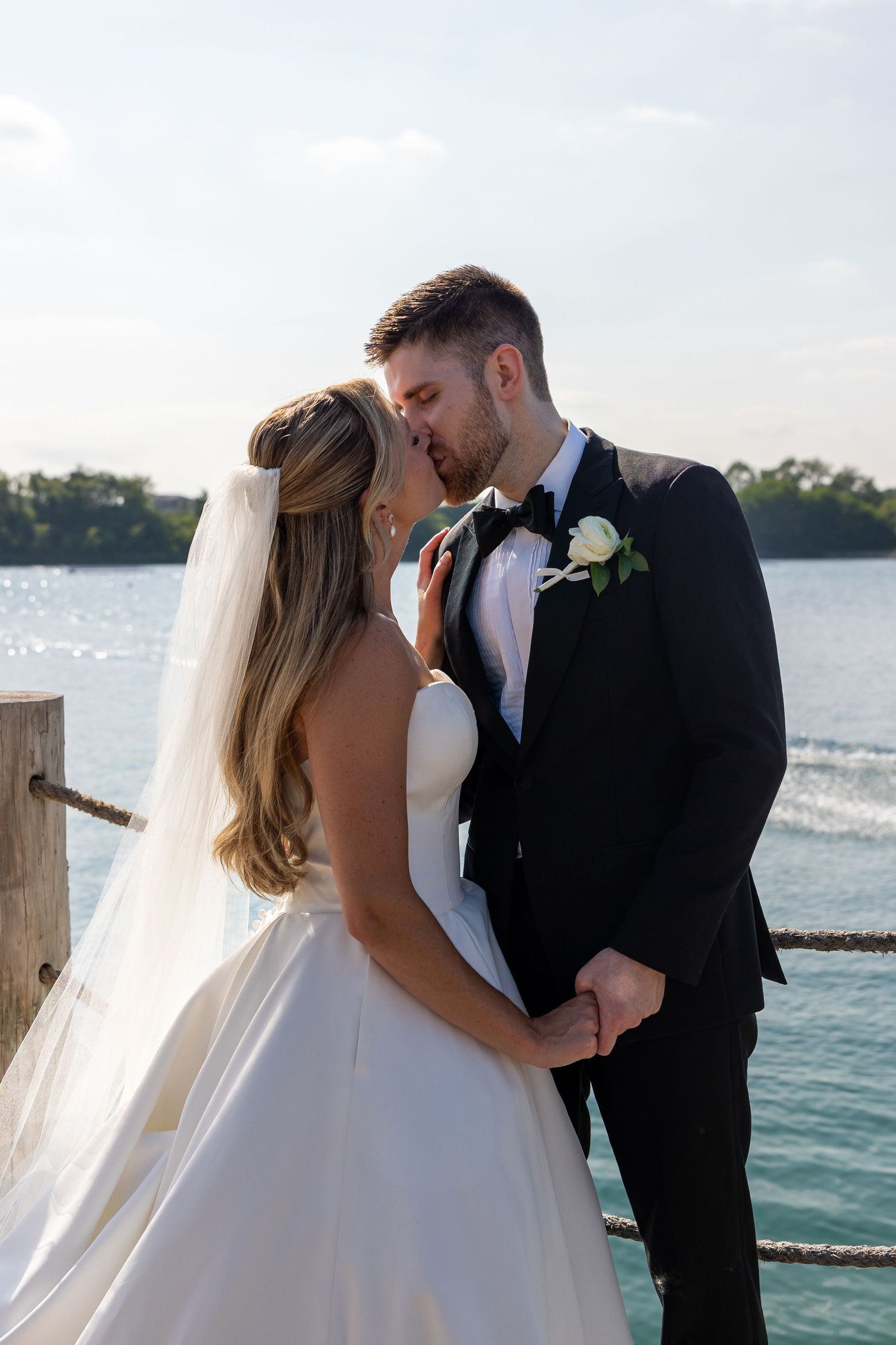 Newlyweds share an intimate moment by the waterfront with bride in white gown and groom in black tuxedo.