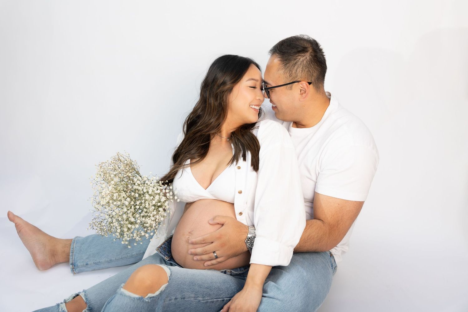Romantic maternity portrait with couple in white and denim against light background.