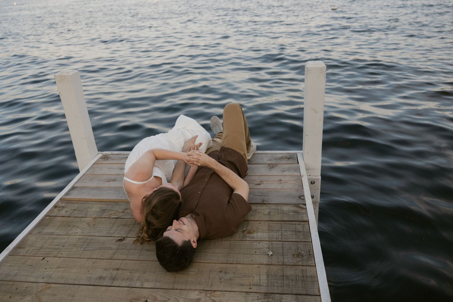 Someone lies peacefully on a wooden dock over dark rippling water during a tranquil moment.