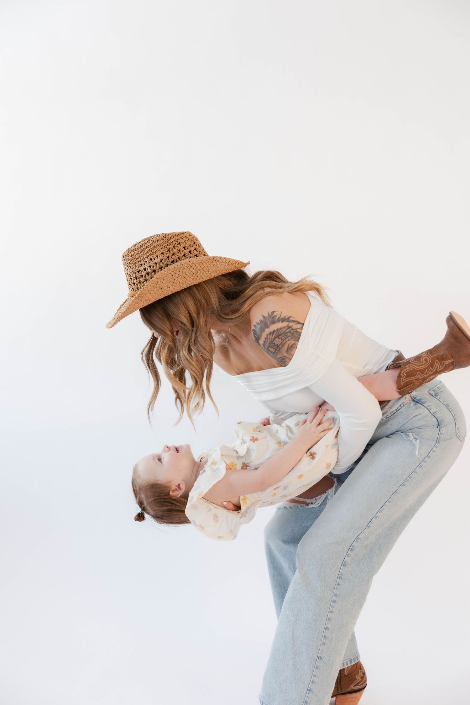 Playful lifestyle portrait of parent and child in matching neutral tones against white background.