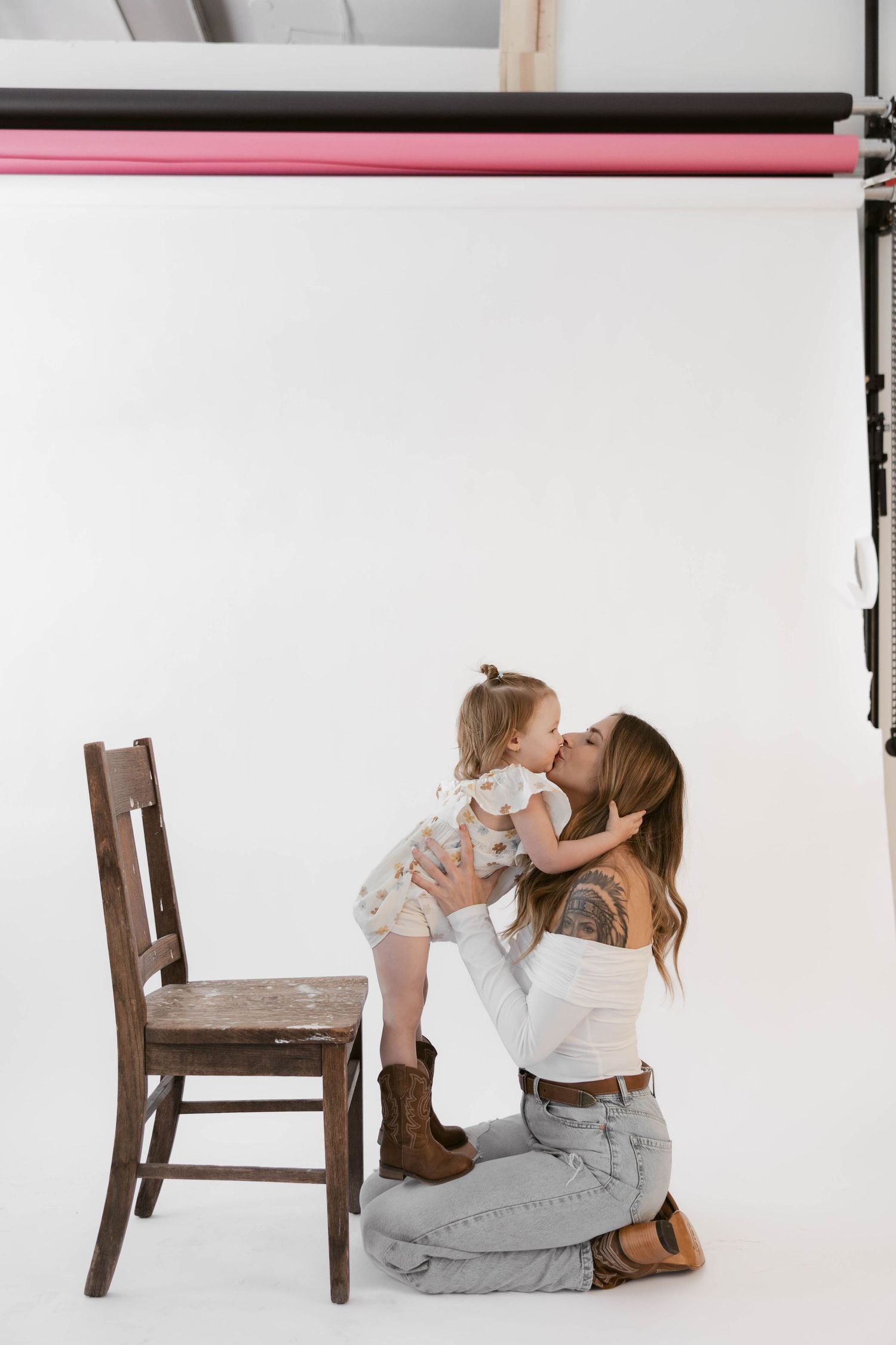 Sweet moment captured in studio with embracing figures by wooden chair against white background.
