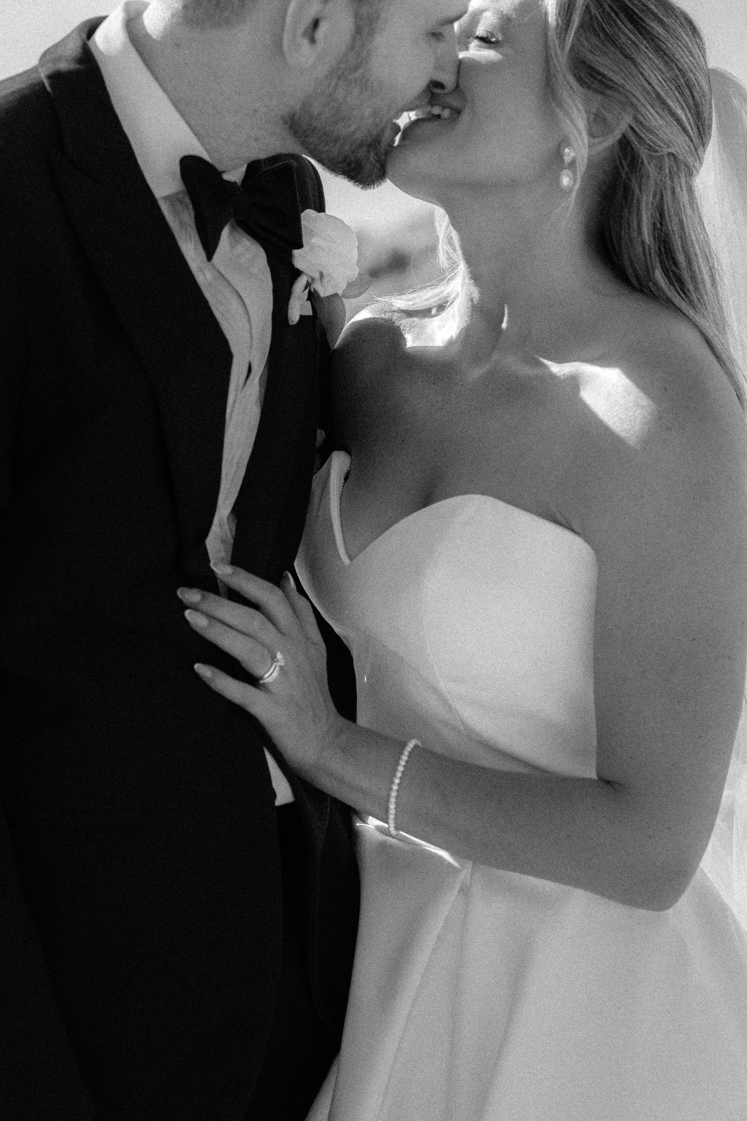Black and white close-up of bride and groom sharing an intimate kiss in formal wedding attire.