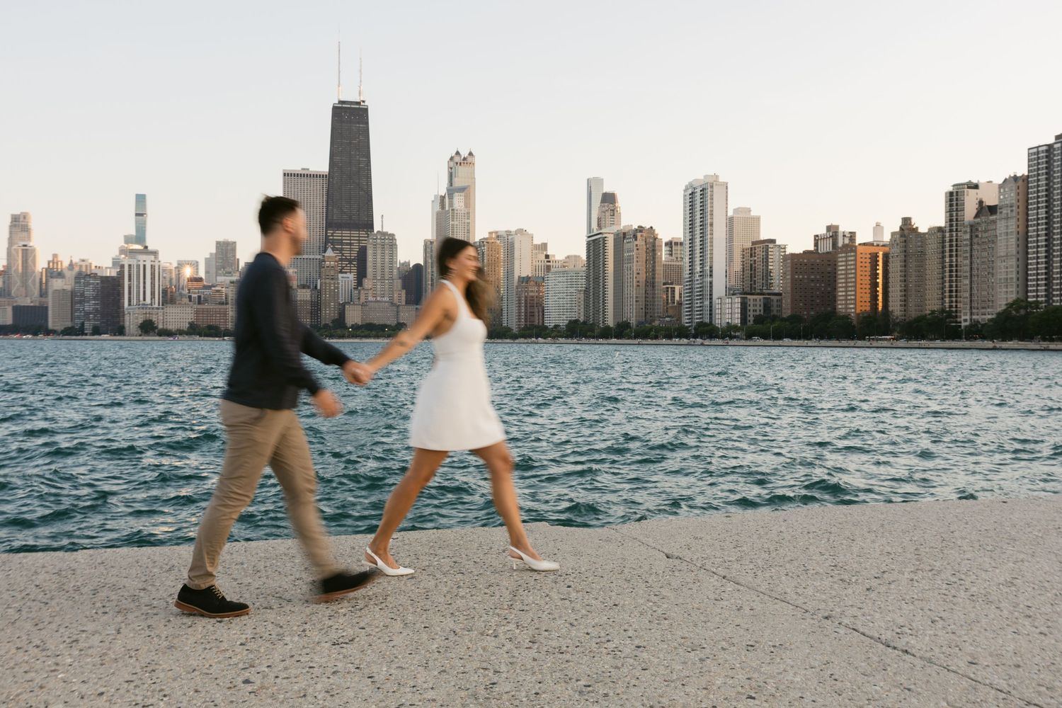 Couple walking along Chicago lakefront with dramatic city skyline view.