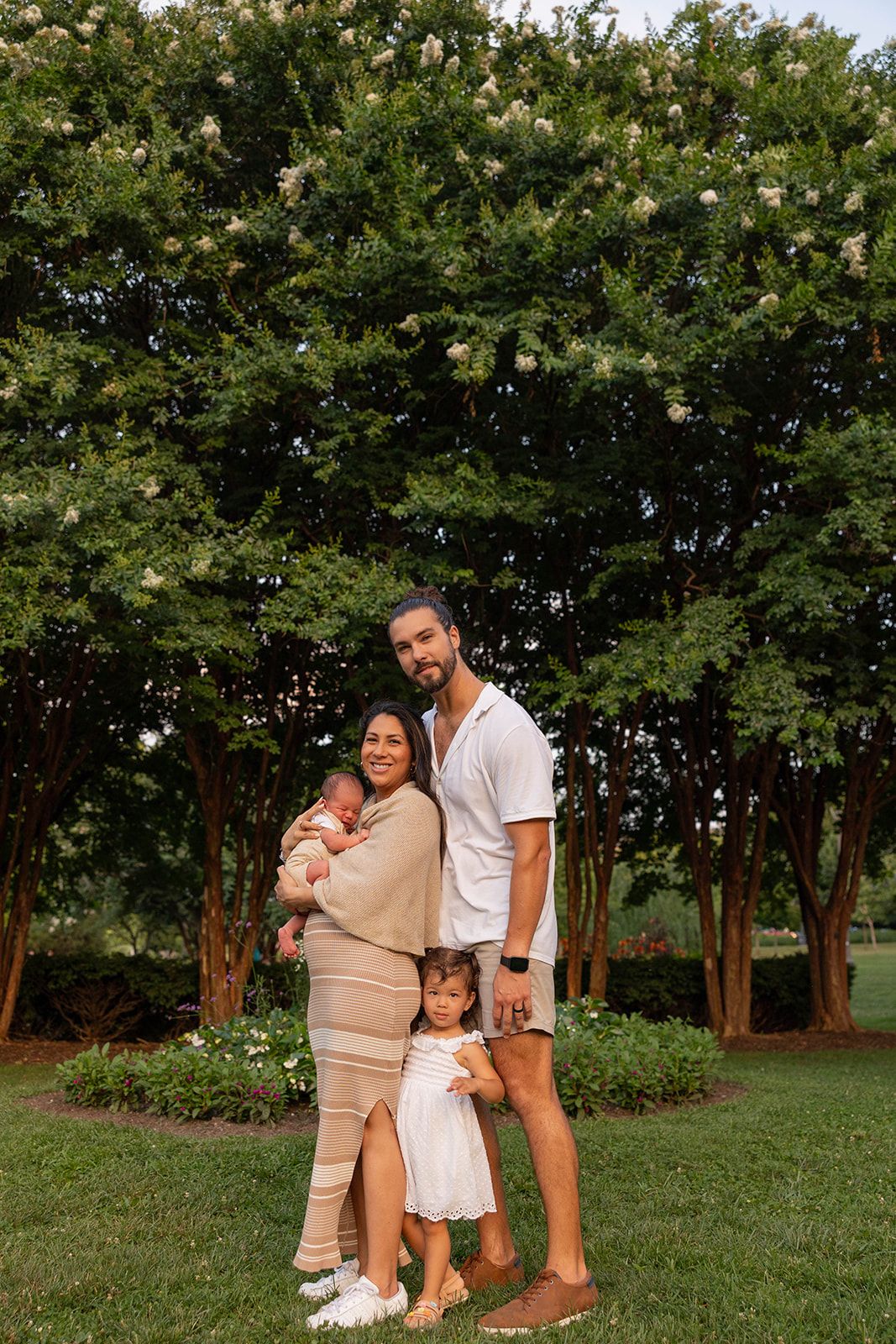 A family of four poses together for a photo outdoors against a backdrop of lush trees.