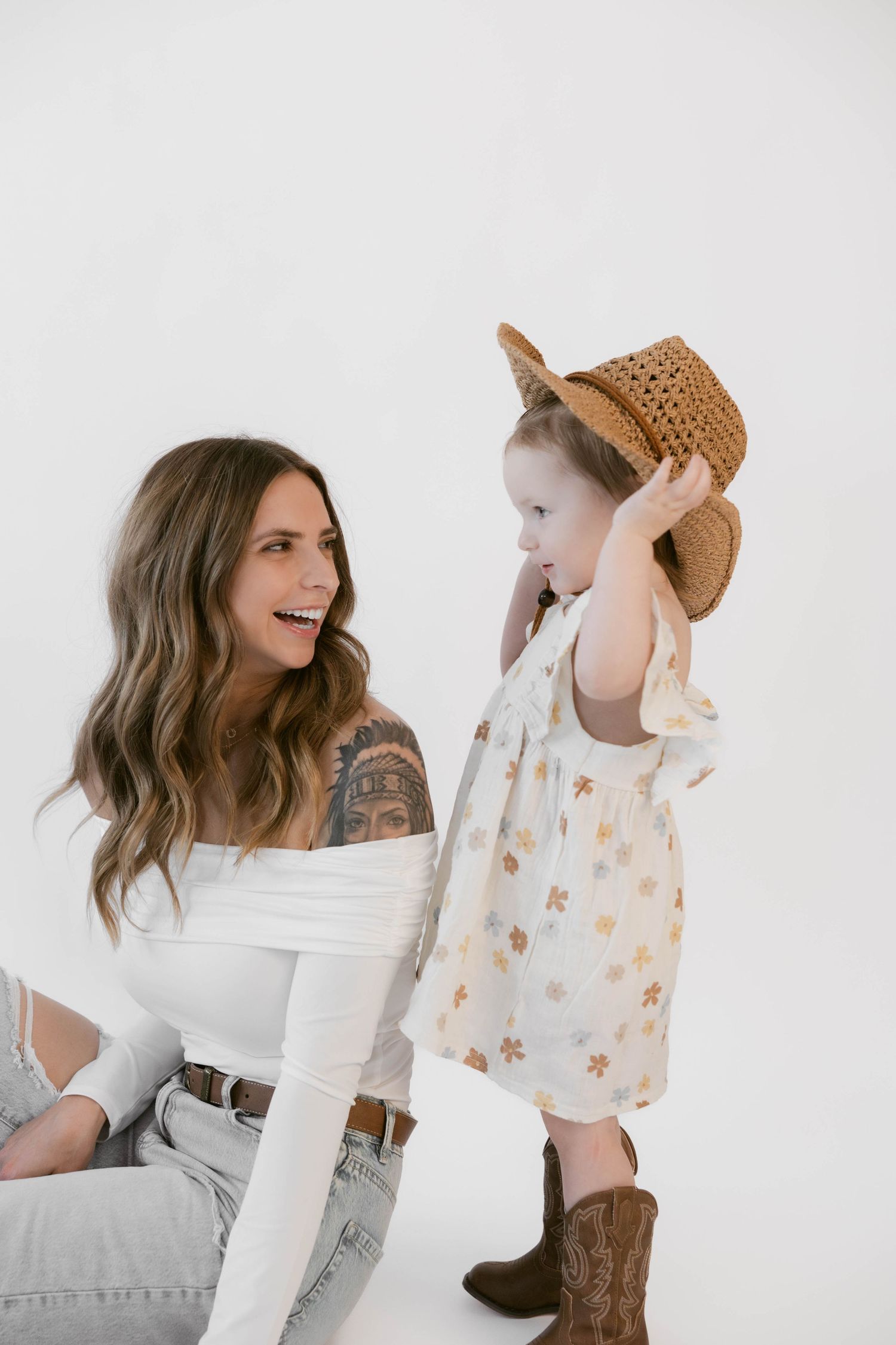 Two people in cowboy hats share laughter during a casual photoshoot on white background.