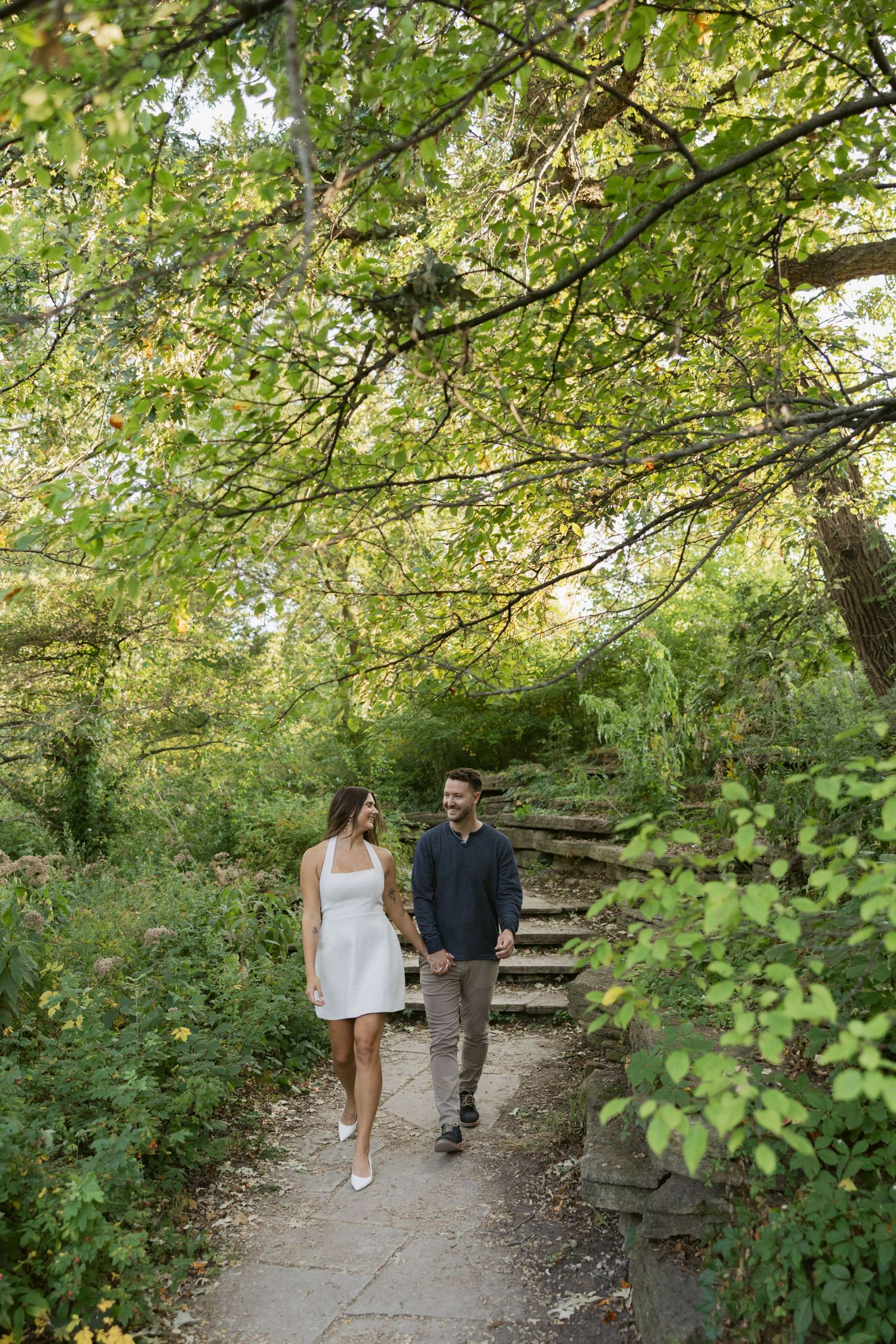Couple walking along a tree-lined path in a park during golden hour.