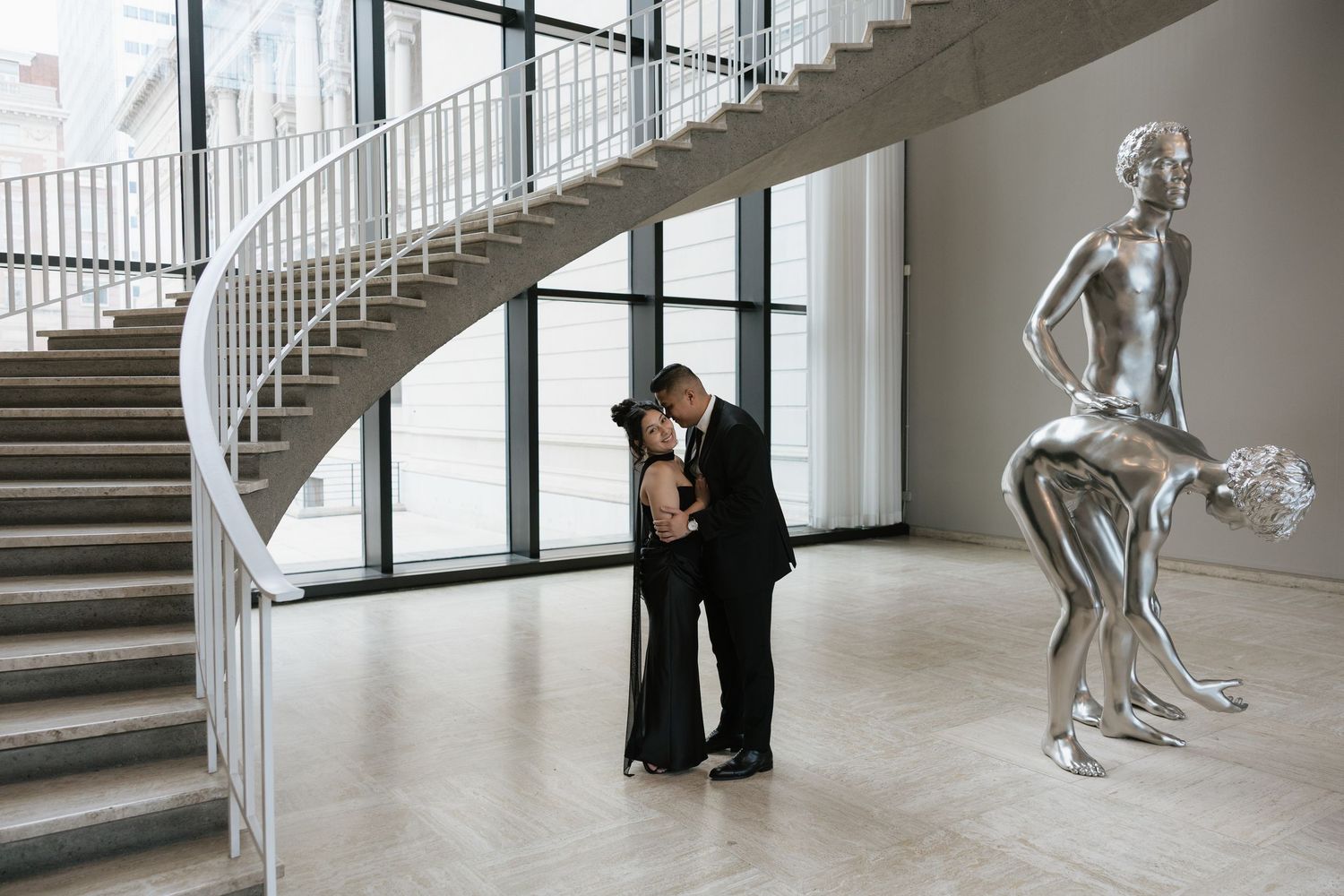 A romantic photoshoot in a modern interior with spiral staircase and silver statue decoration.