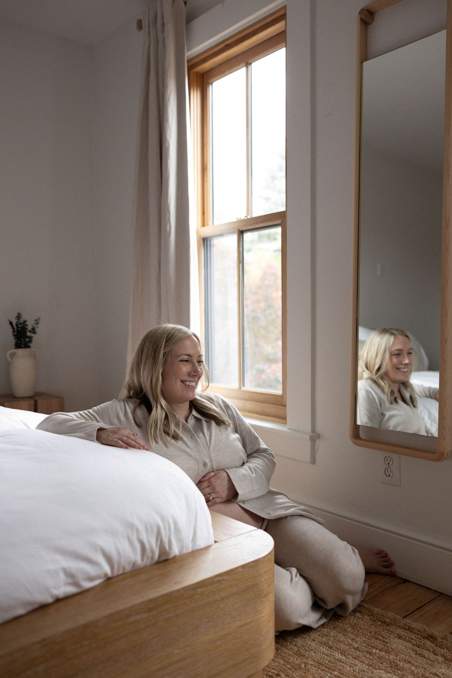 A relaxed scene in a bright bedroom with someone lounging against white bedding near a sunlit window.
