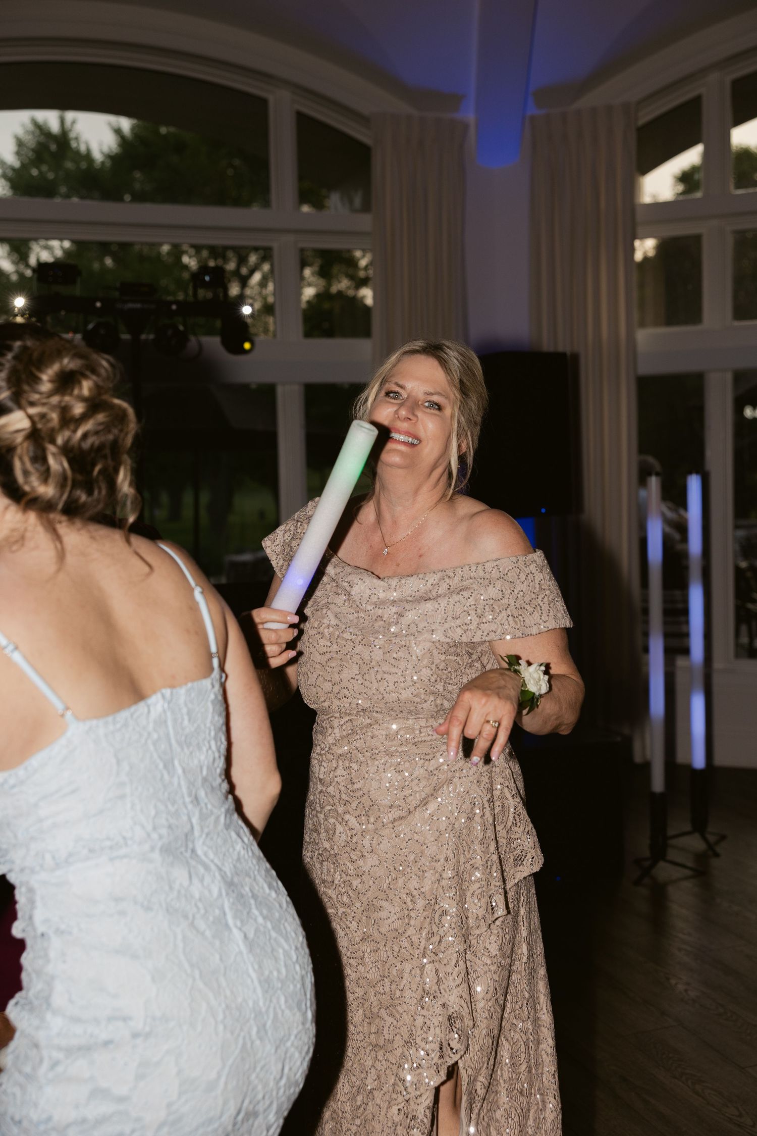 Wedding guests dance exuberantly with glow sticks under blue lighting at an evening reception.
