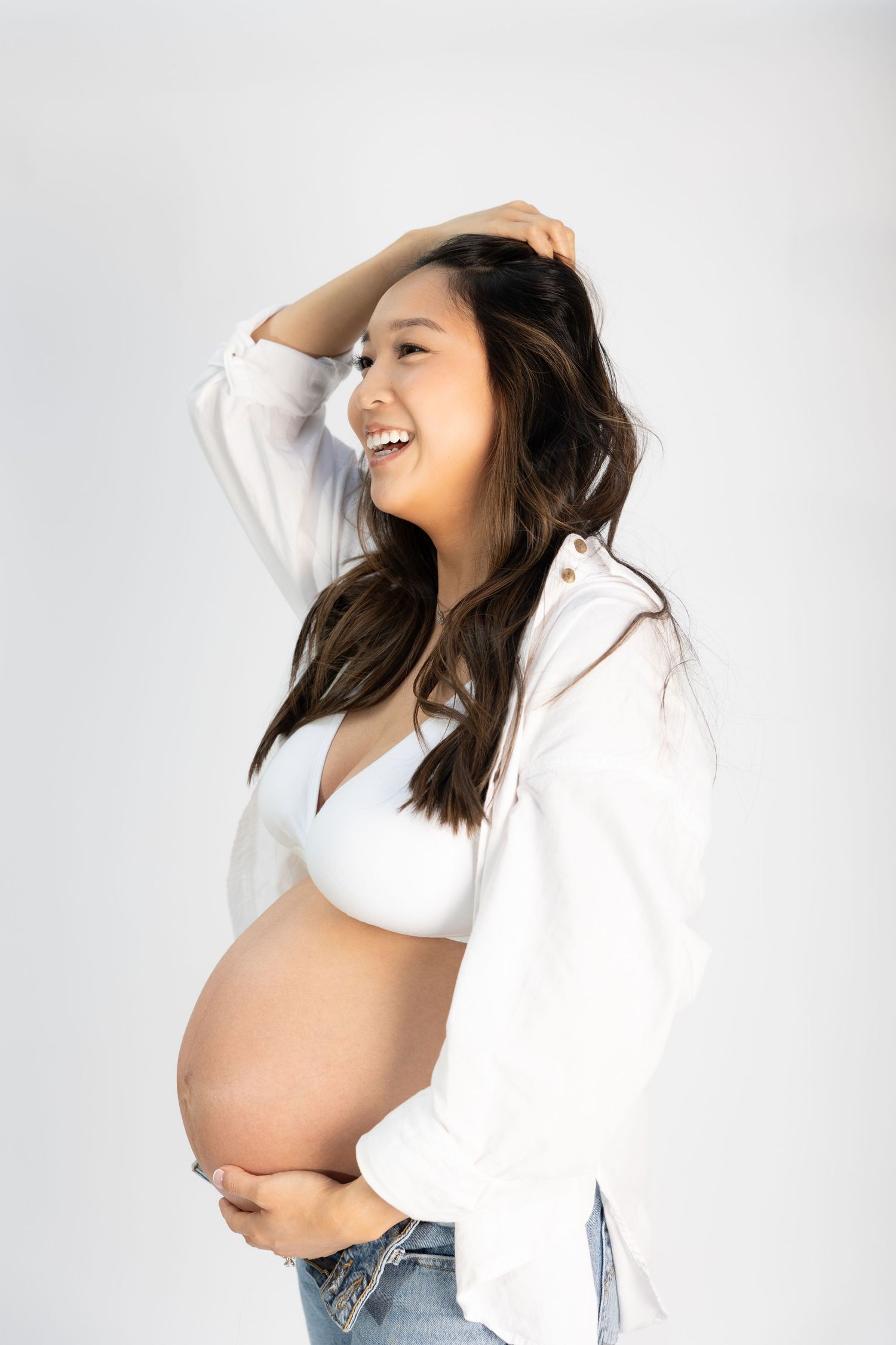 Joyful maternity photo with woman laughing in white top and jeans.