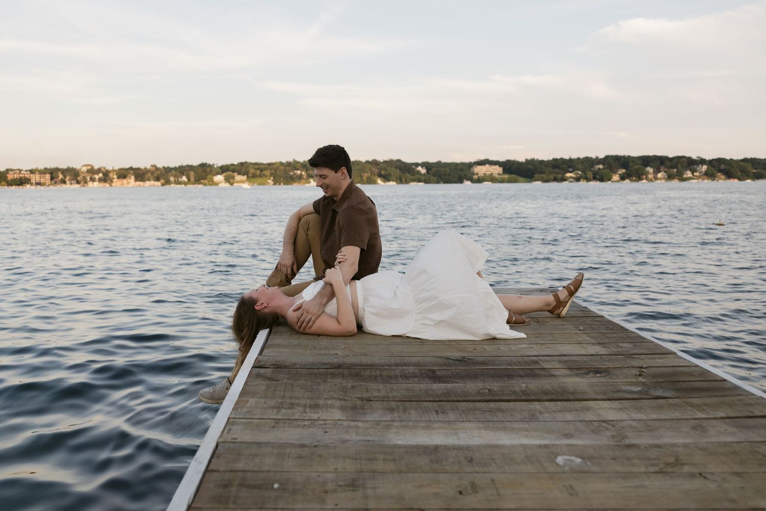 Couple relaxing together on a wooden dock over calm lake waters at sunset.