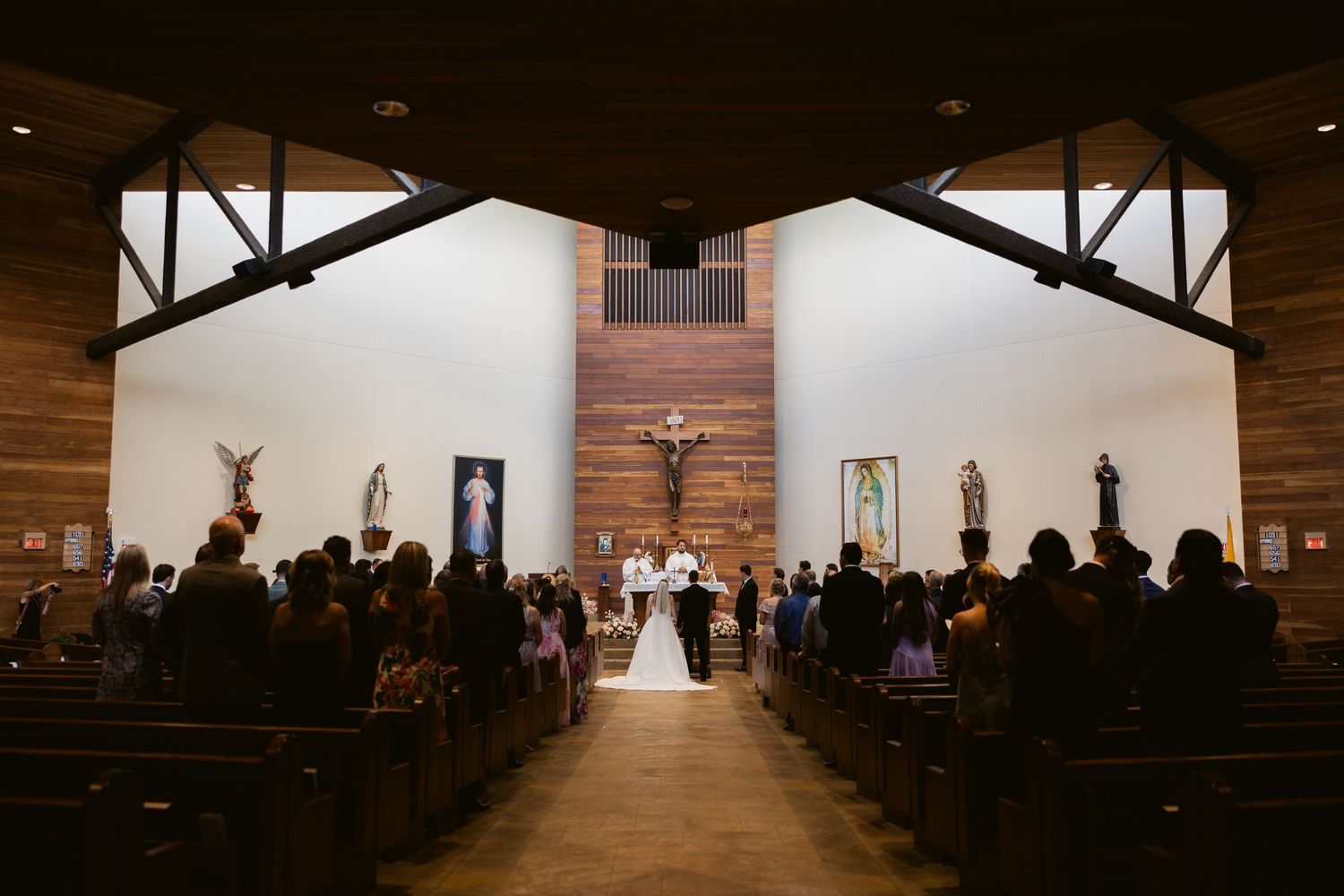 Interior wide shot of a wedding ceremony in a rustic wooden church sanctuary with exposed beams and gathered guests.