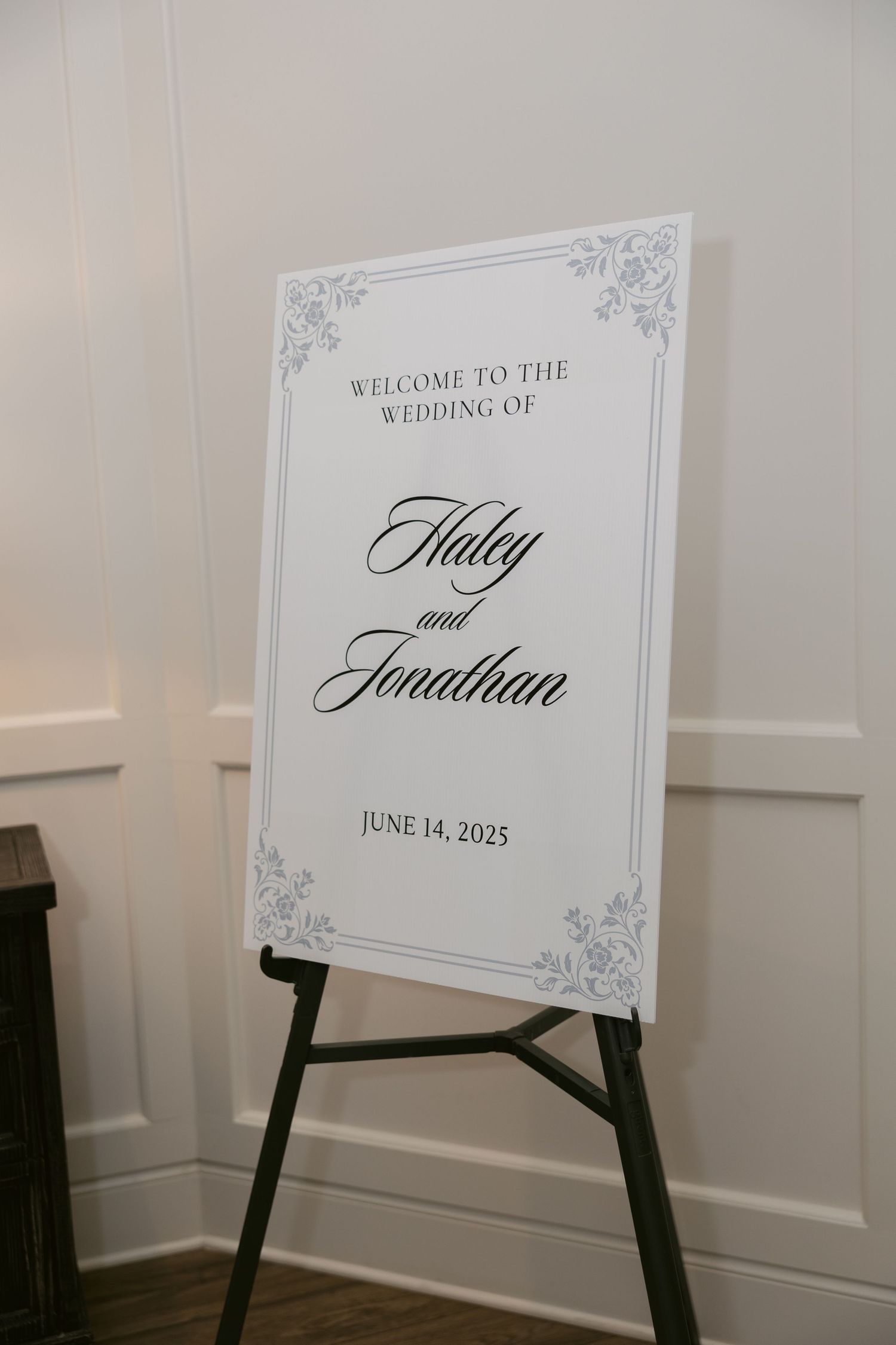 Elegant wedding welcome sign on easel with ornate frame design displaying couple's names and date.