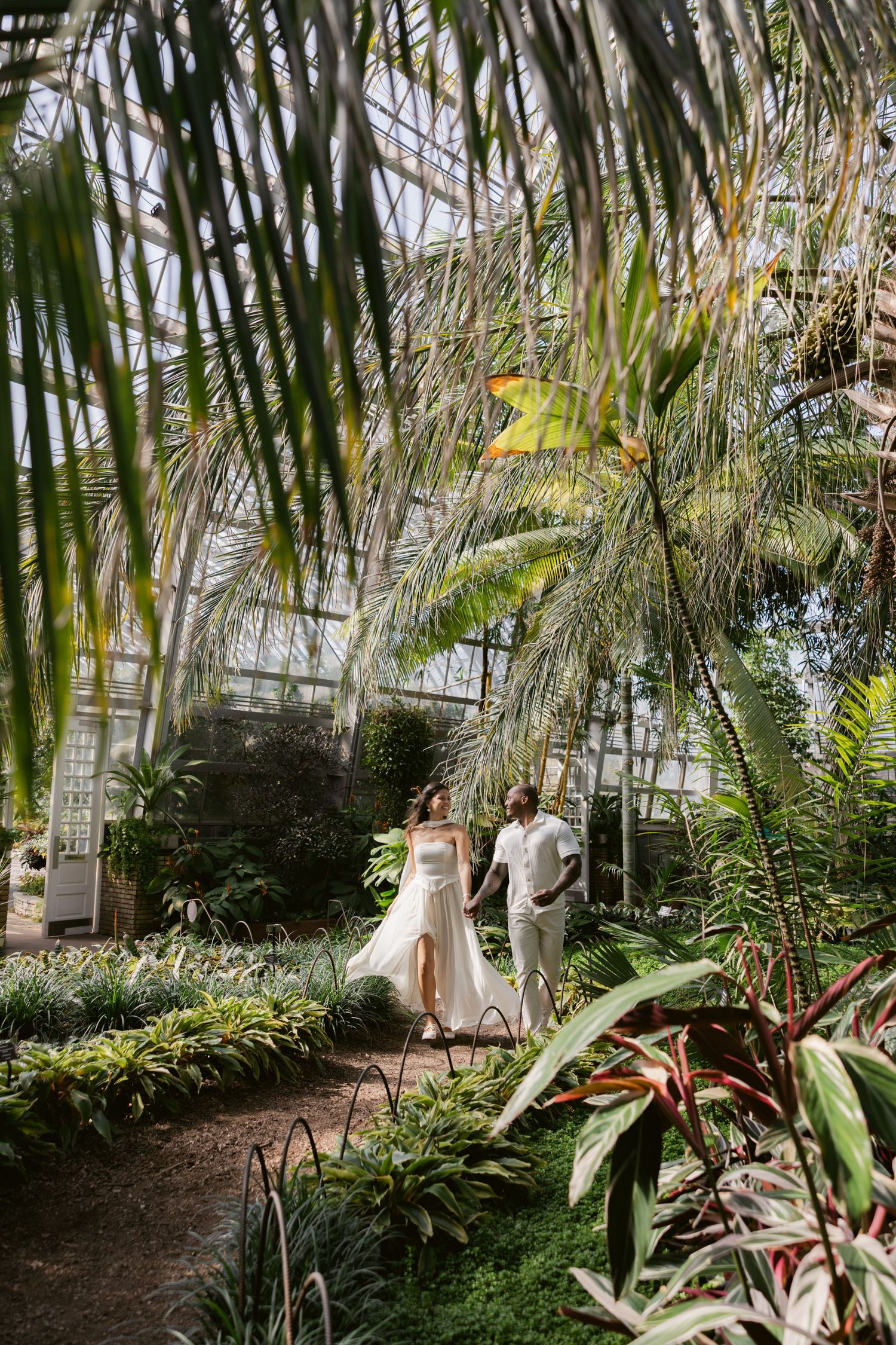 Romantic photoshoot in a tropical greenhouse with palm fronds and exotic plants.