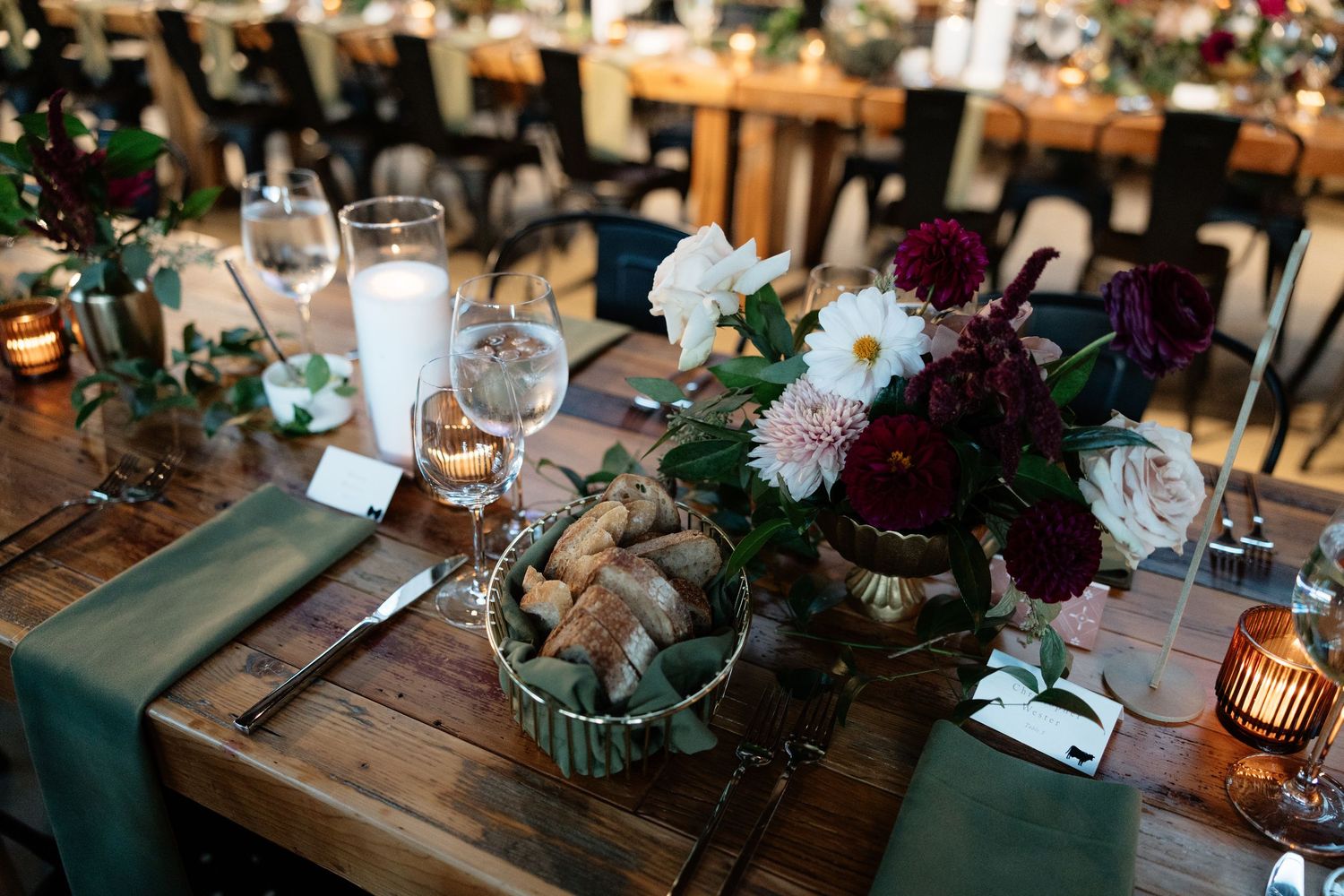 Rustic wedding reception table settings with dark floral centerpieces and candlelight accents.