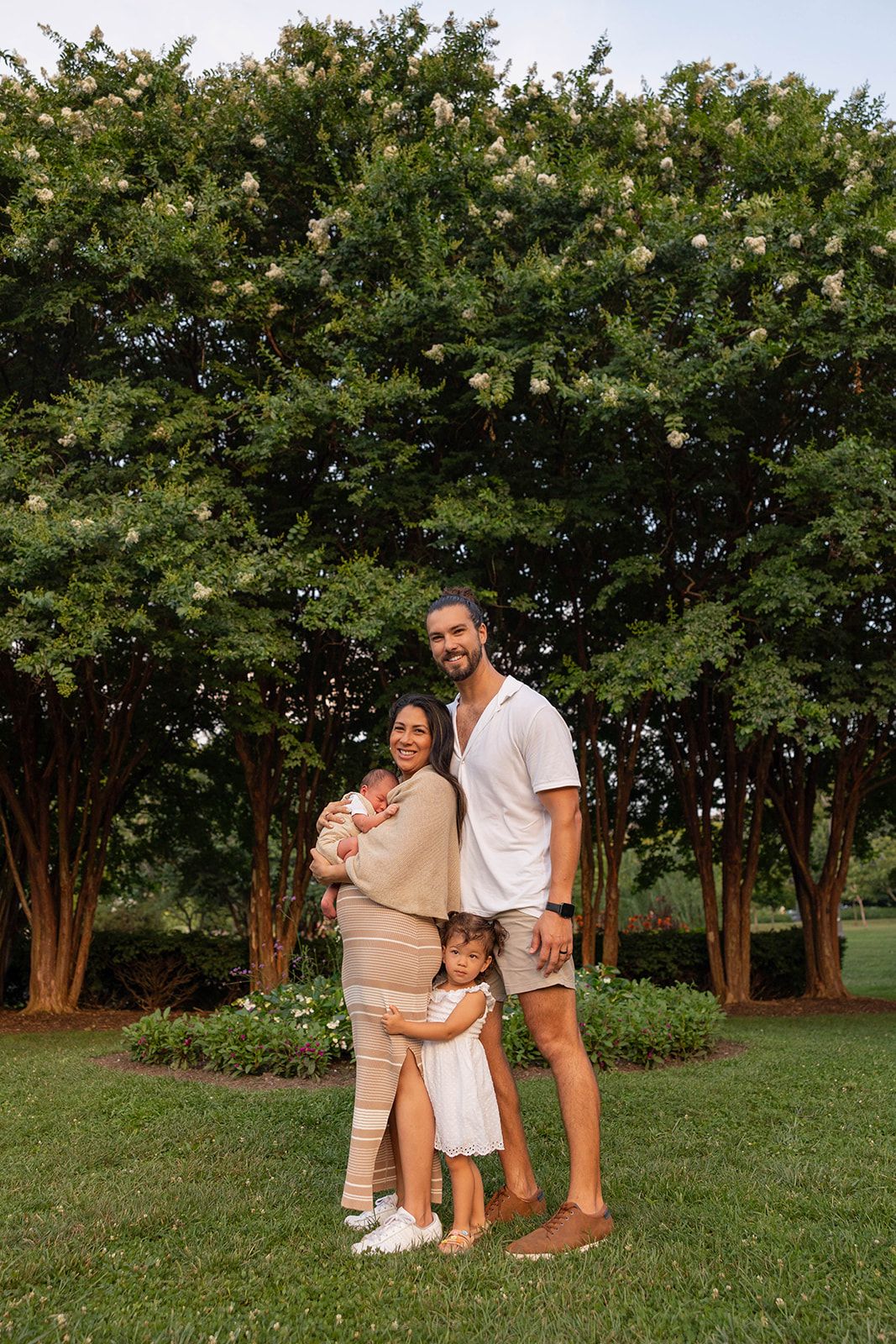 A portrait of a young couple with two children standing under flowering trees in a garden.
