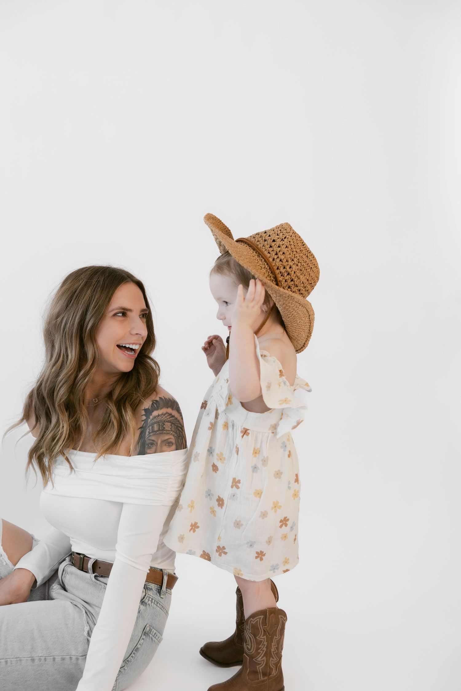 A pair in western-inspired outfits share a joyful moment against a white backdrop.