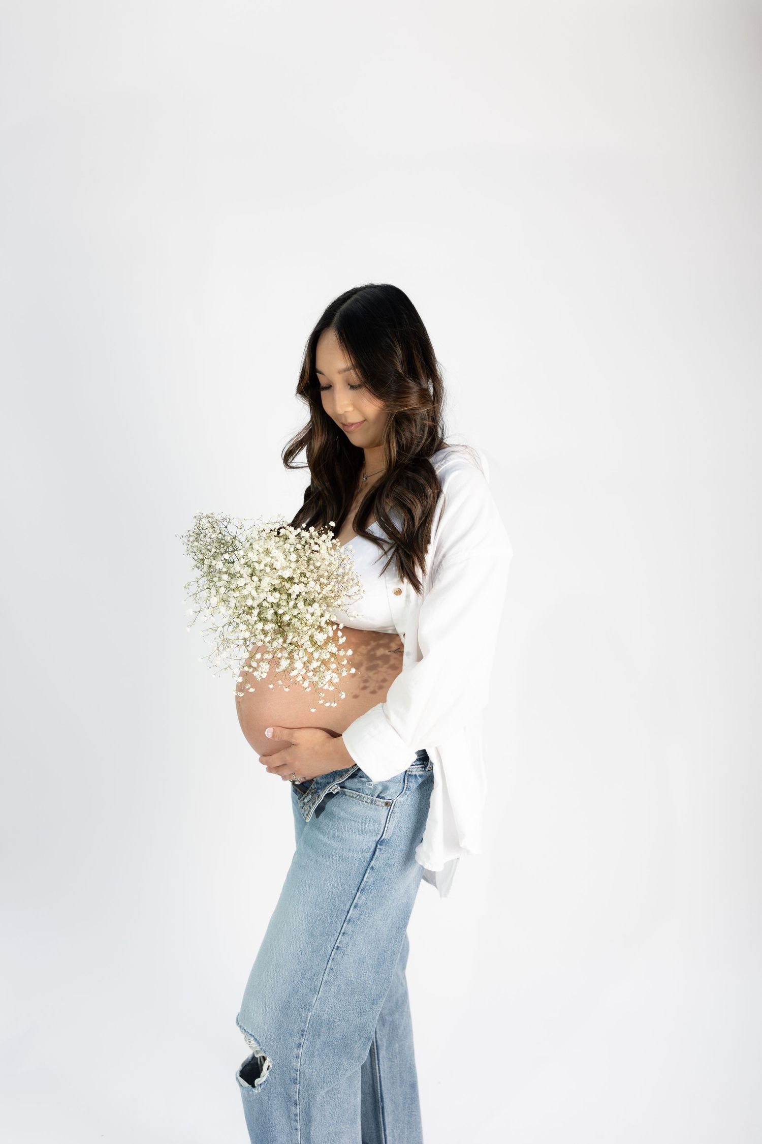 Side profile maternity shot with woman holding baby's breath flowers in casual outfit.