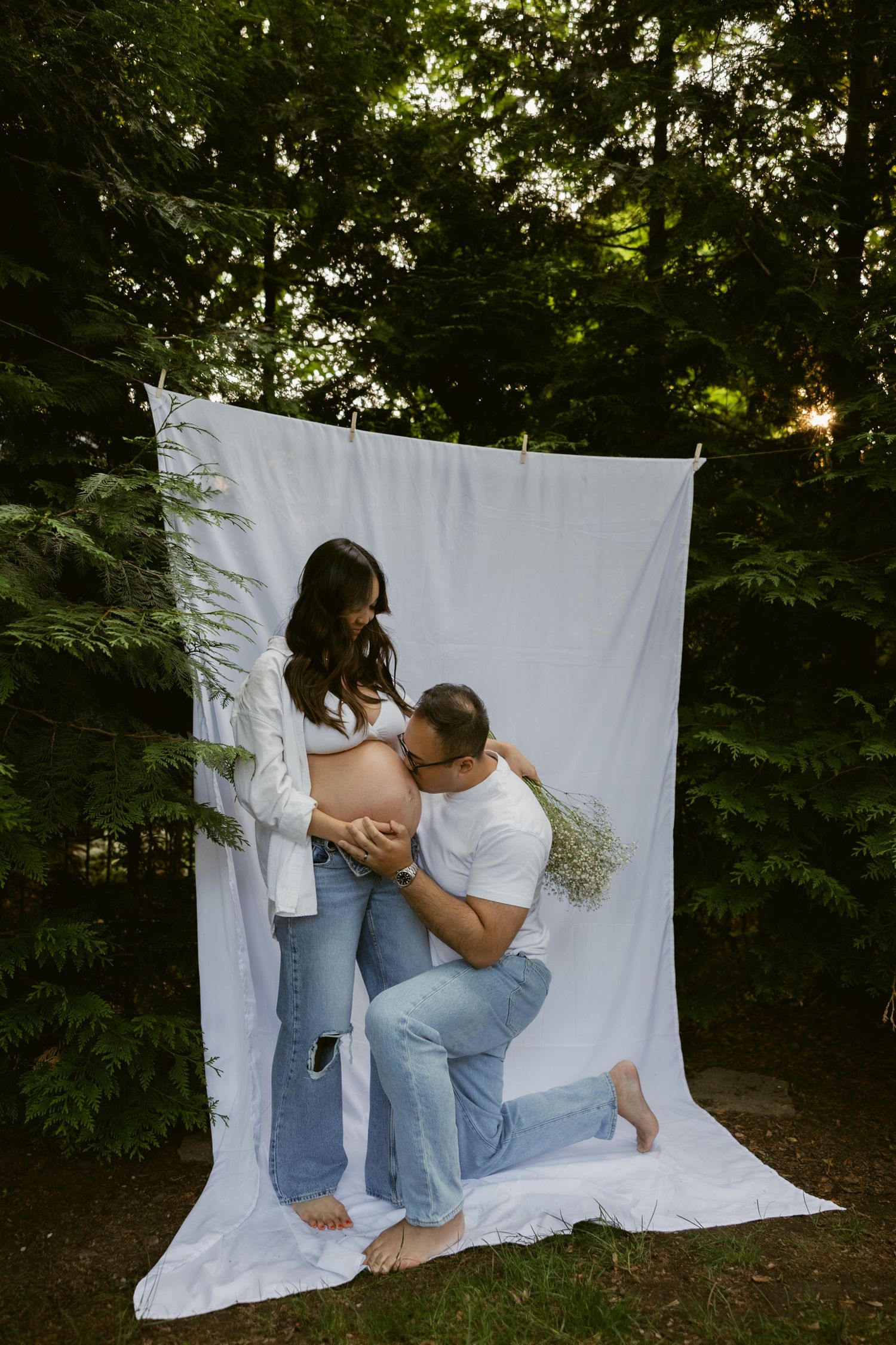 A playful maternity photoshoot moment captured against a white backdrop in nature.