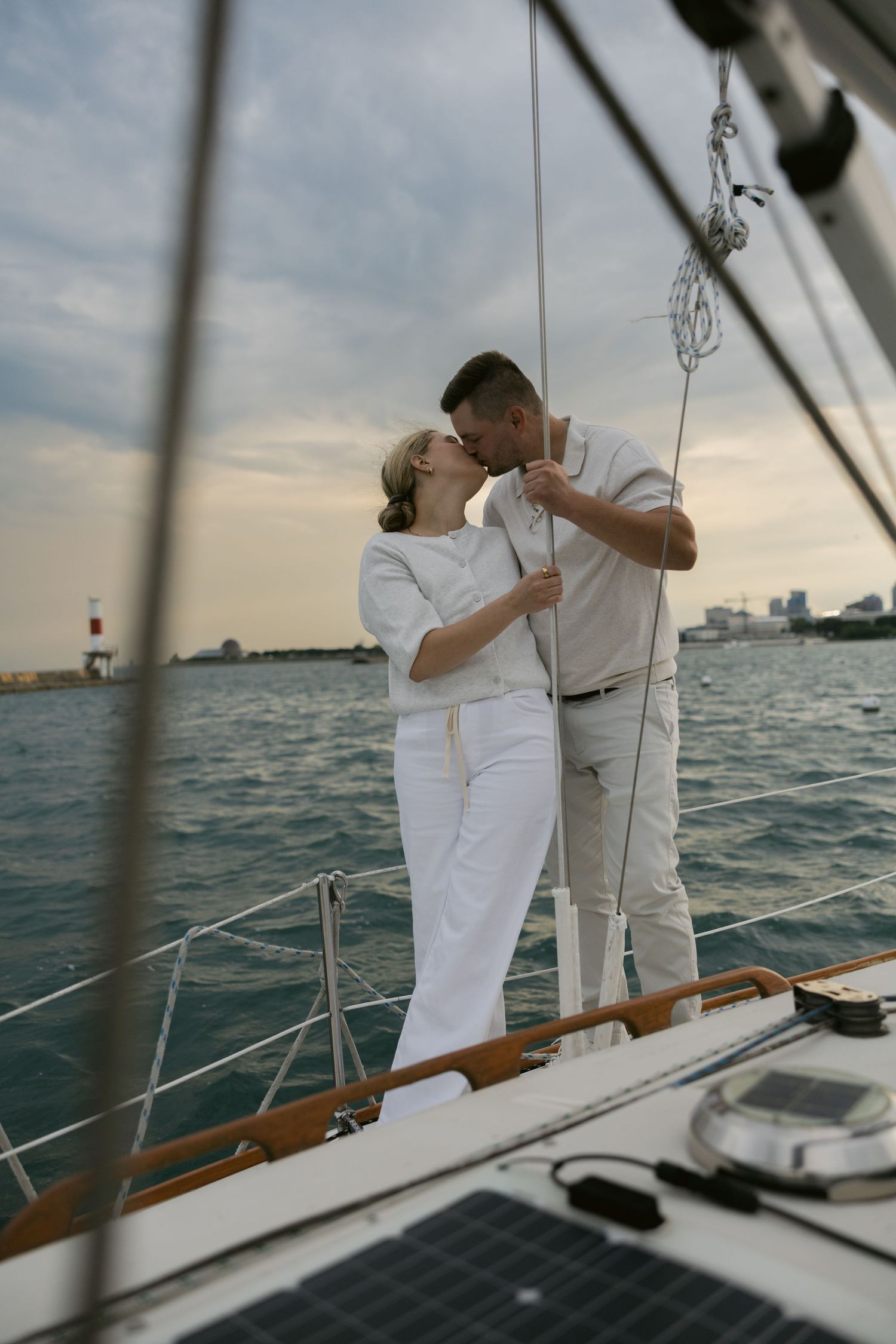 Couple in white clothing sharing intimate moments aboard a sailboat during sunset on the water.