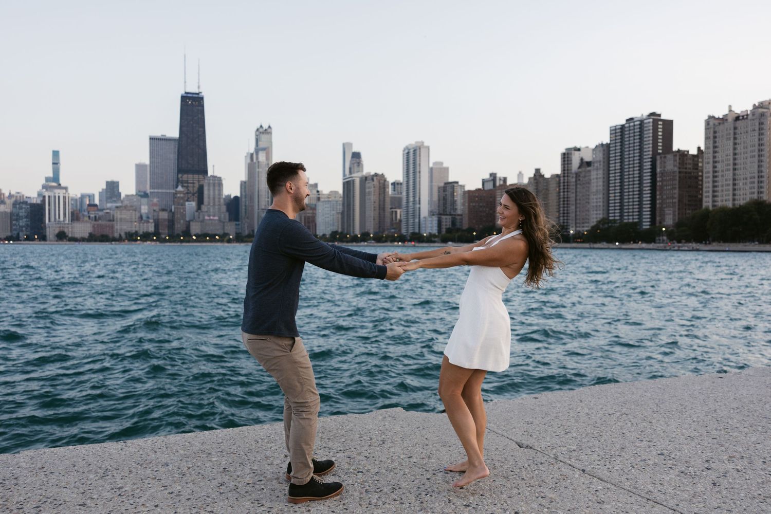 Playful engagement photo with Chicago skyline and Lake Michigan as backdrop.