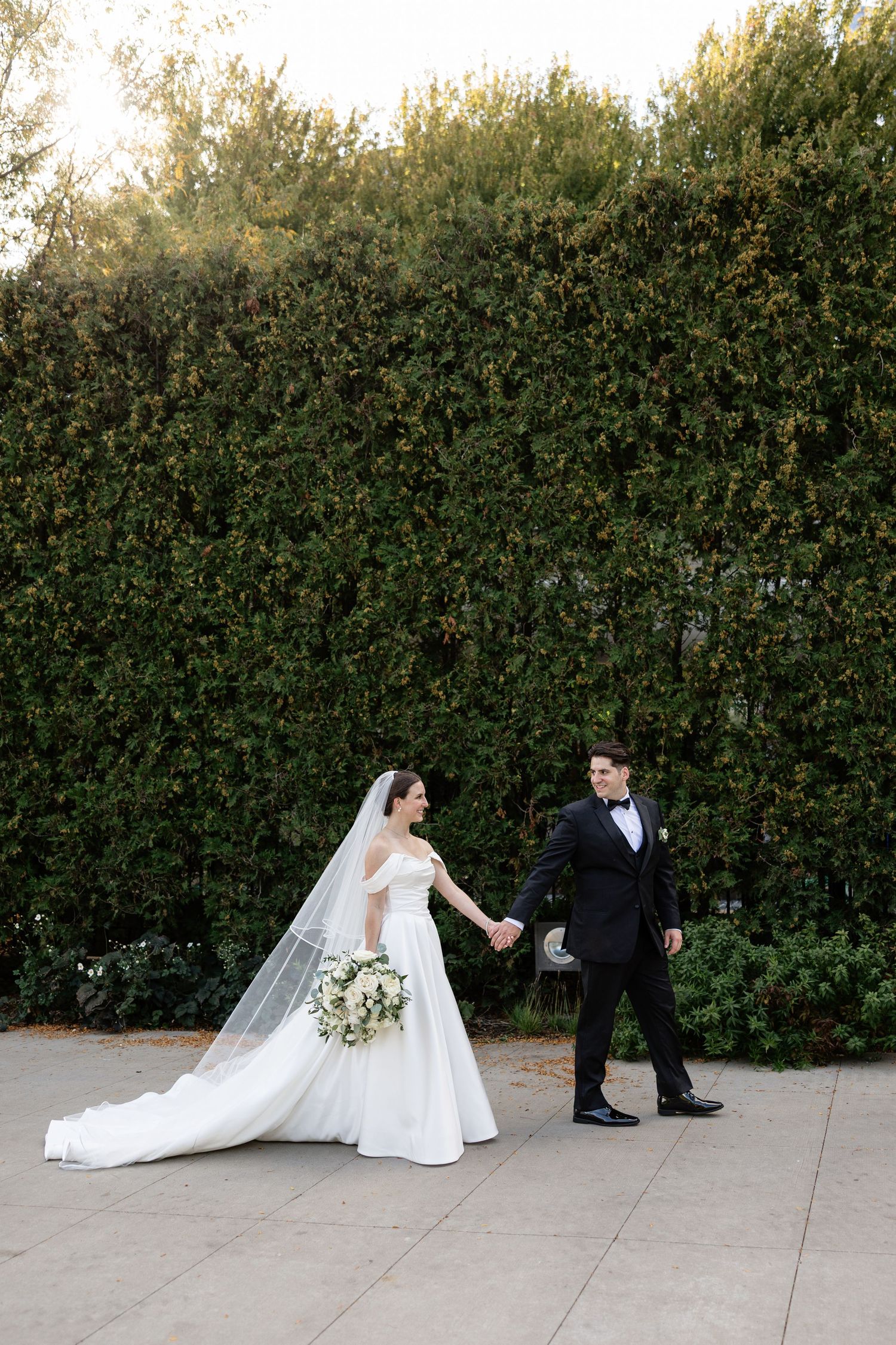 A sequence of wedding photos showing a couple walking and posing together on a stone path beside a green hedge.