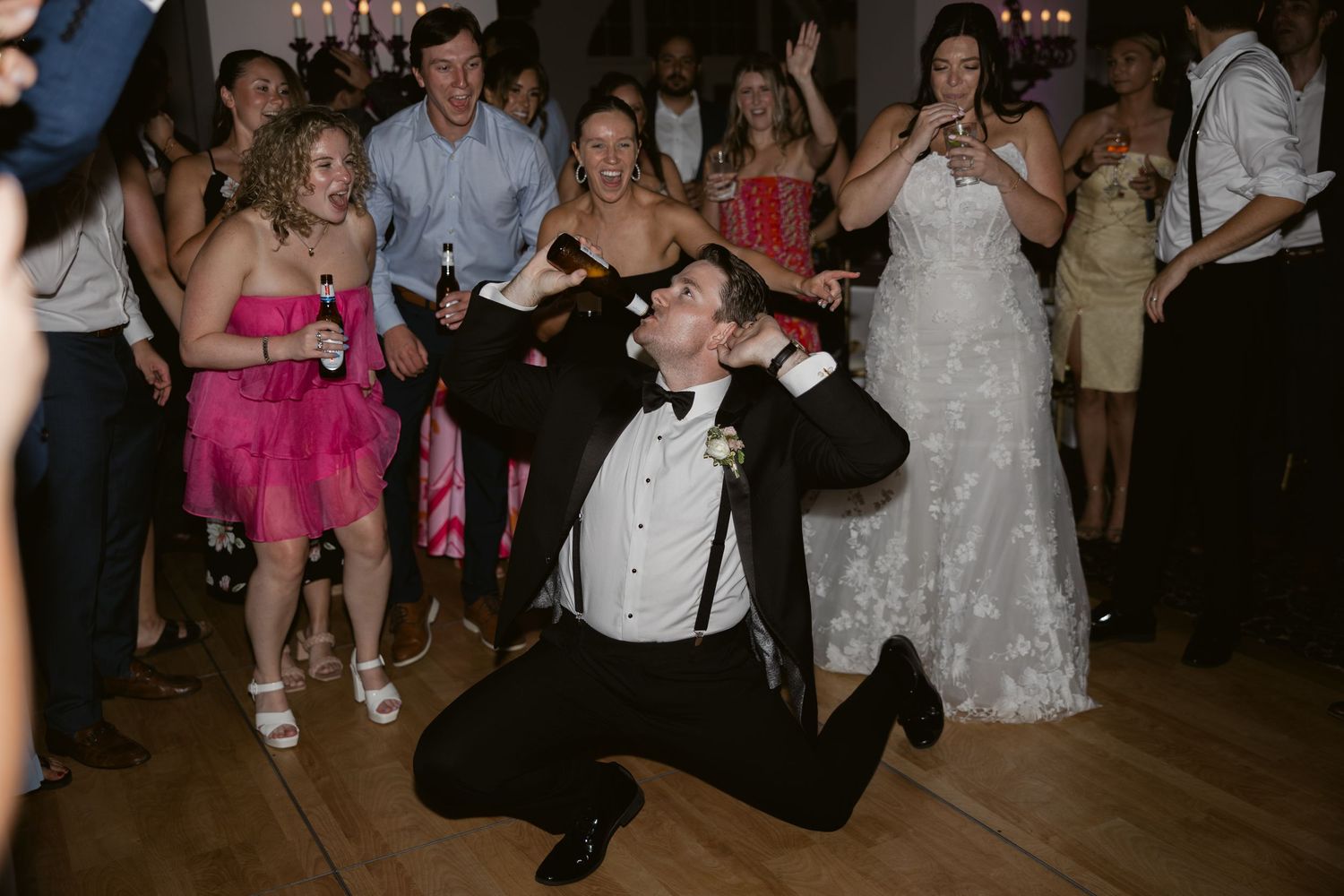Wedding guests dance and celebrate on a wooden dance floor at a reception with formal attire and energetic movements.