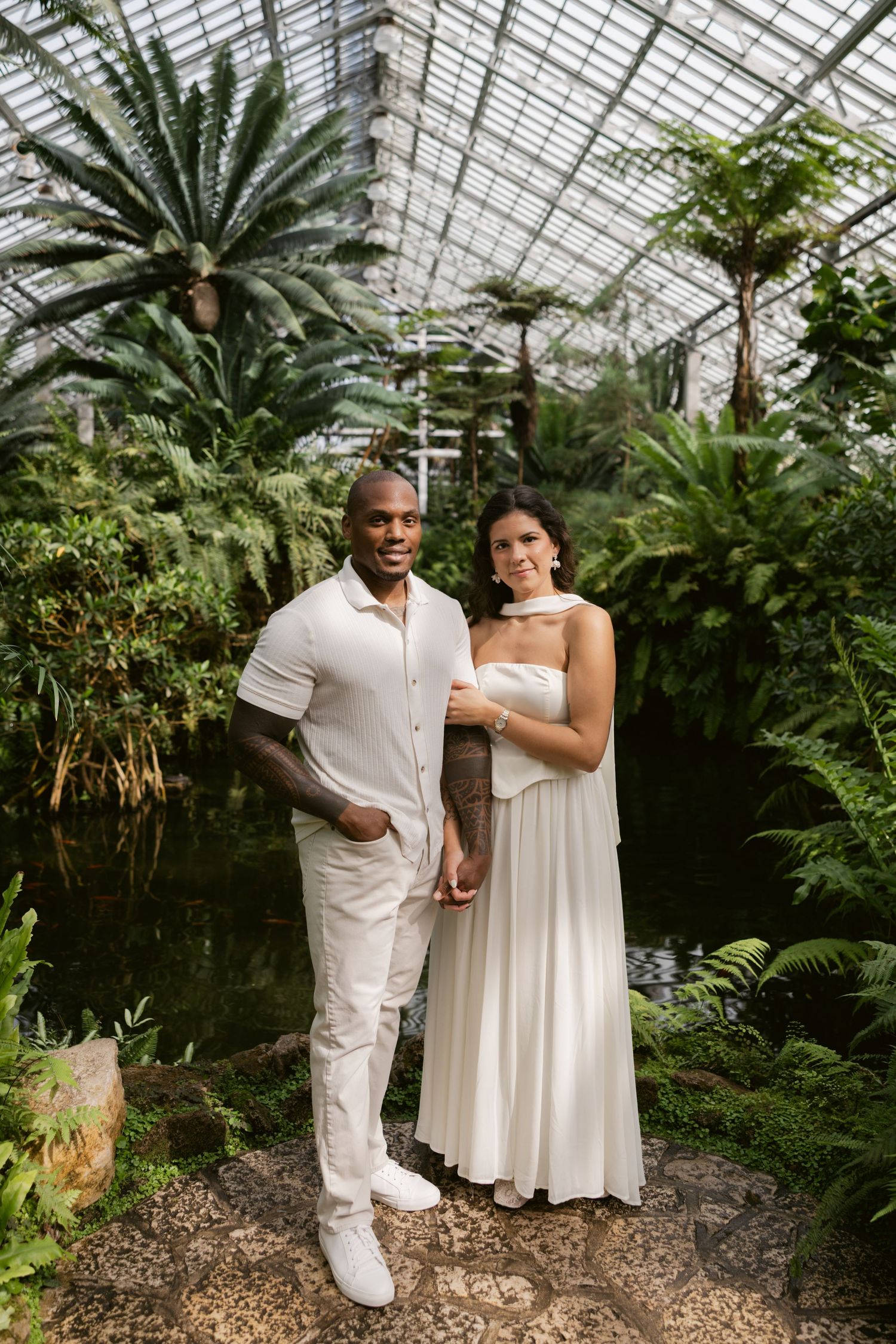 Wedding couple poses in a botanical garden greenhouse surrounded by tropical plants and ferns.