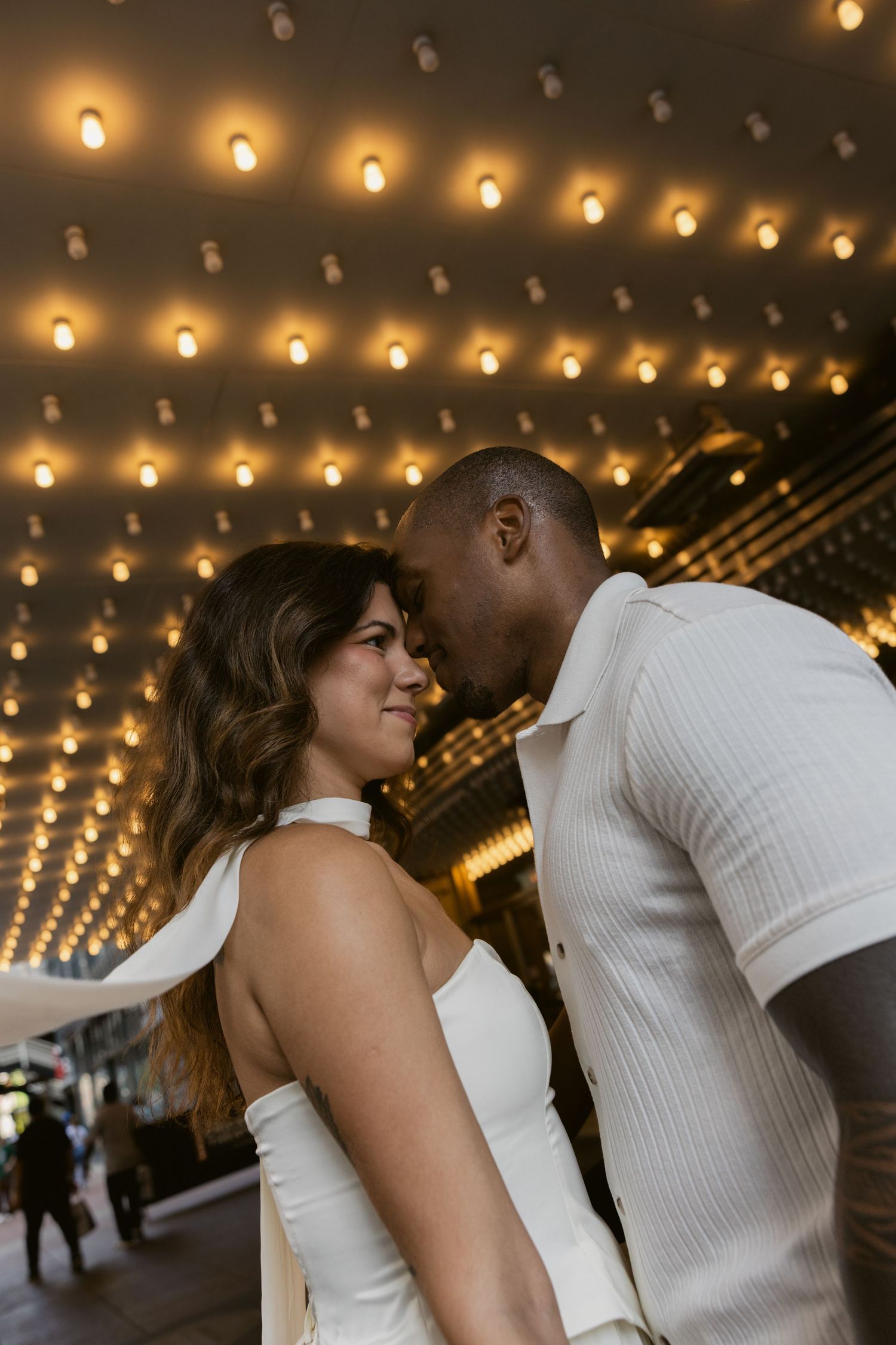 A couple shares an intimate dance under warm theater marquee lights.