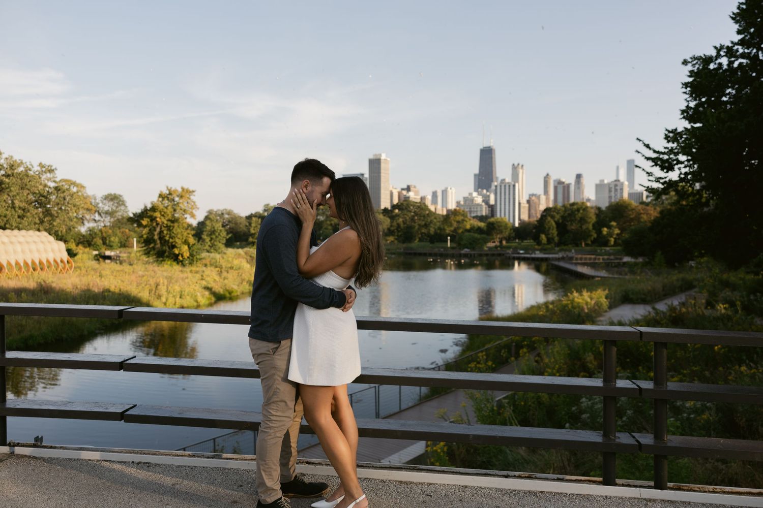 Distant view of Chicago's downtown skyline seen from a park path with autumn foliage bordering a fence railing.