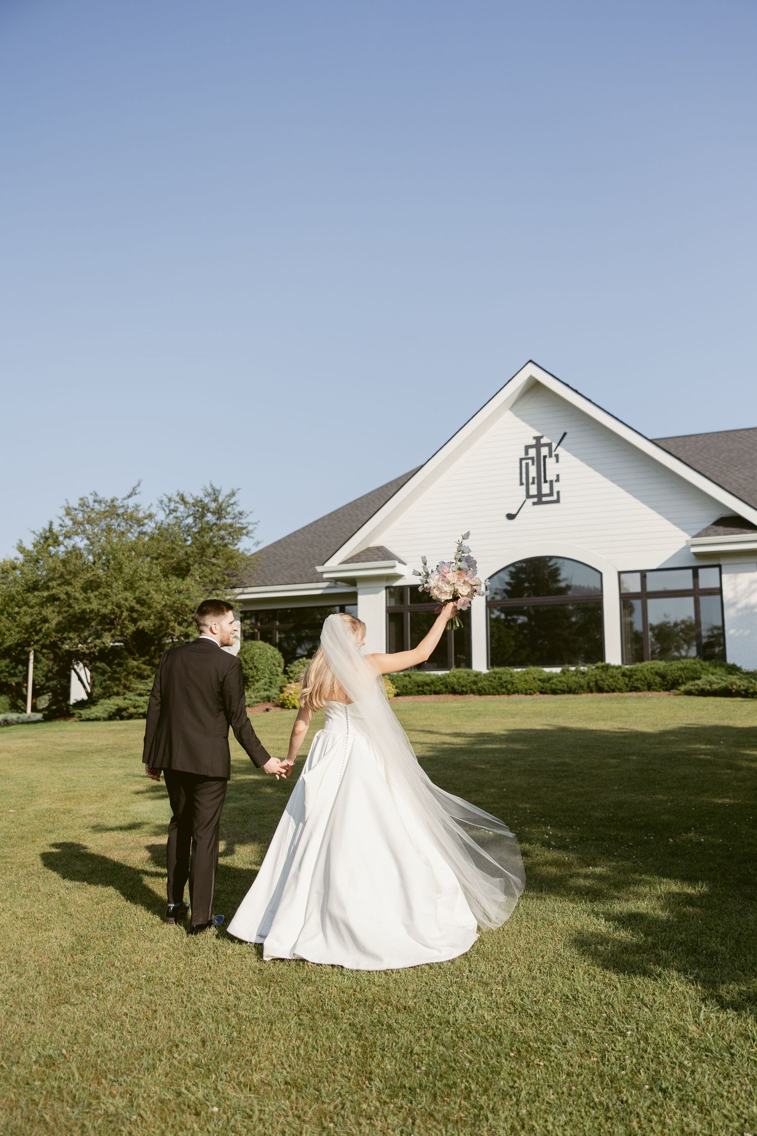 Couple celebrating outside a white clubhouse building on their wedding day.